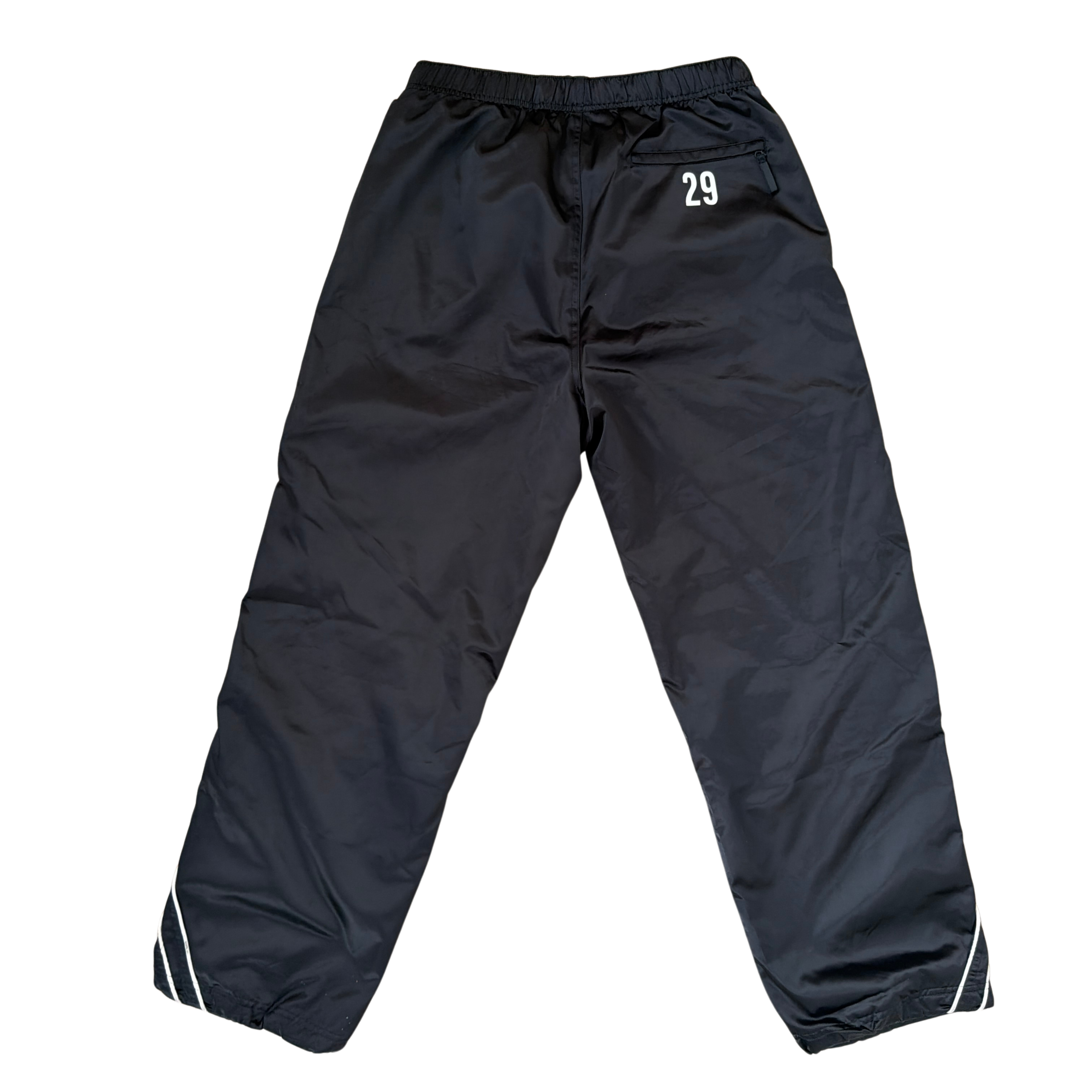 Supreme black satin track pants with white piping, a crest and Supreme logo embroidery at the hip, styled with relaxed legs.