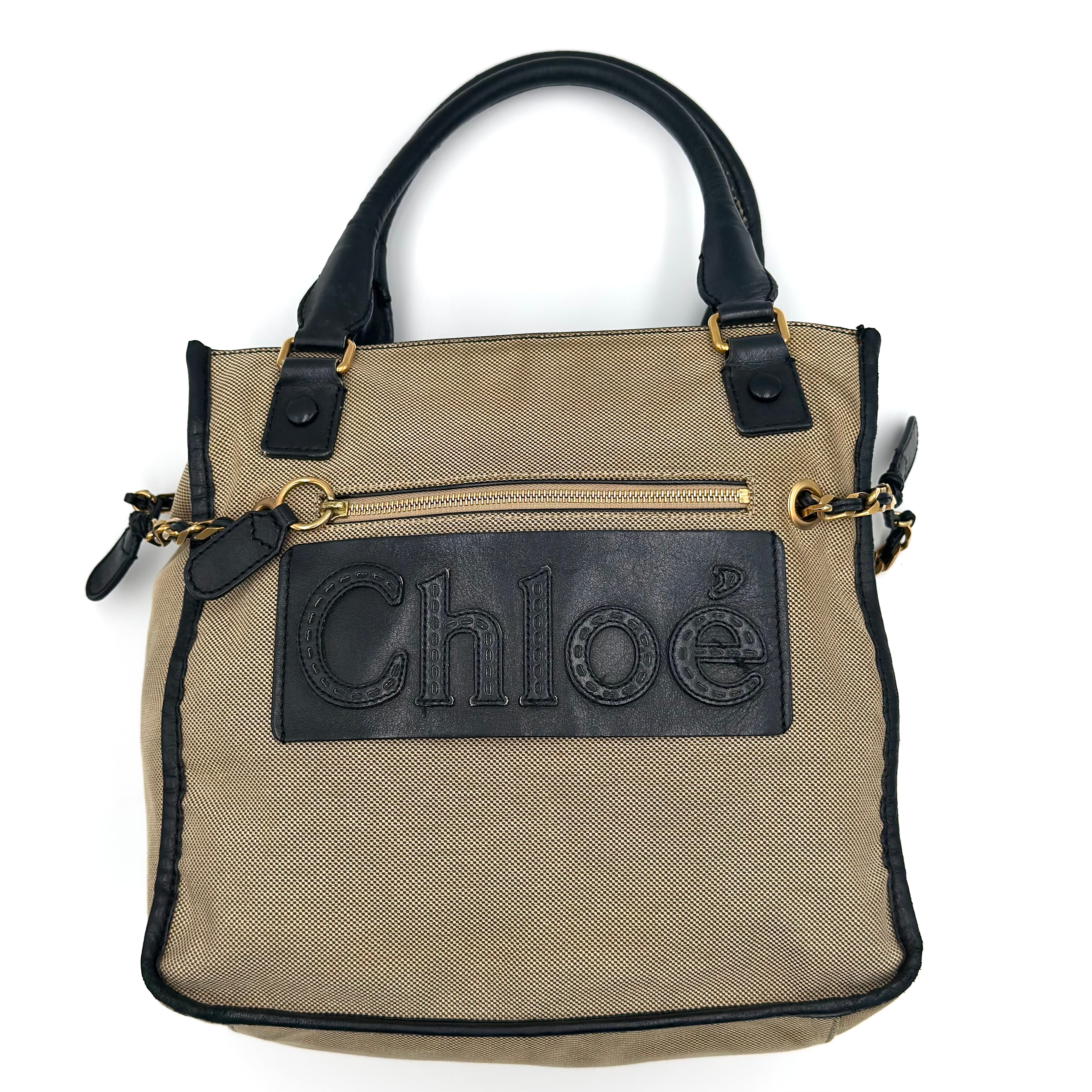 Chloé Harley Handbag in beige canvas with black leather trim, oversized leather logo patch, gold-tone hardware, and spacious zippered interior.