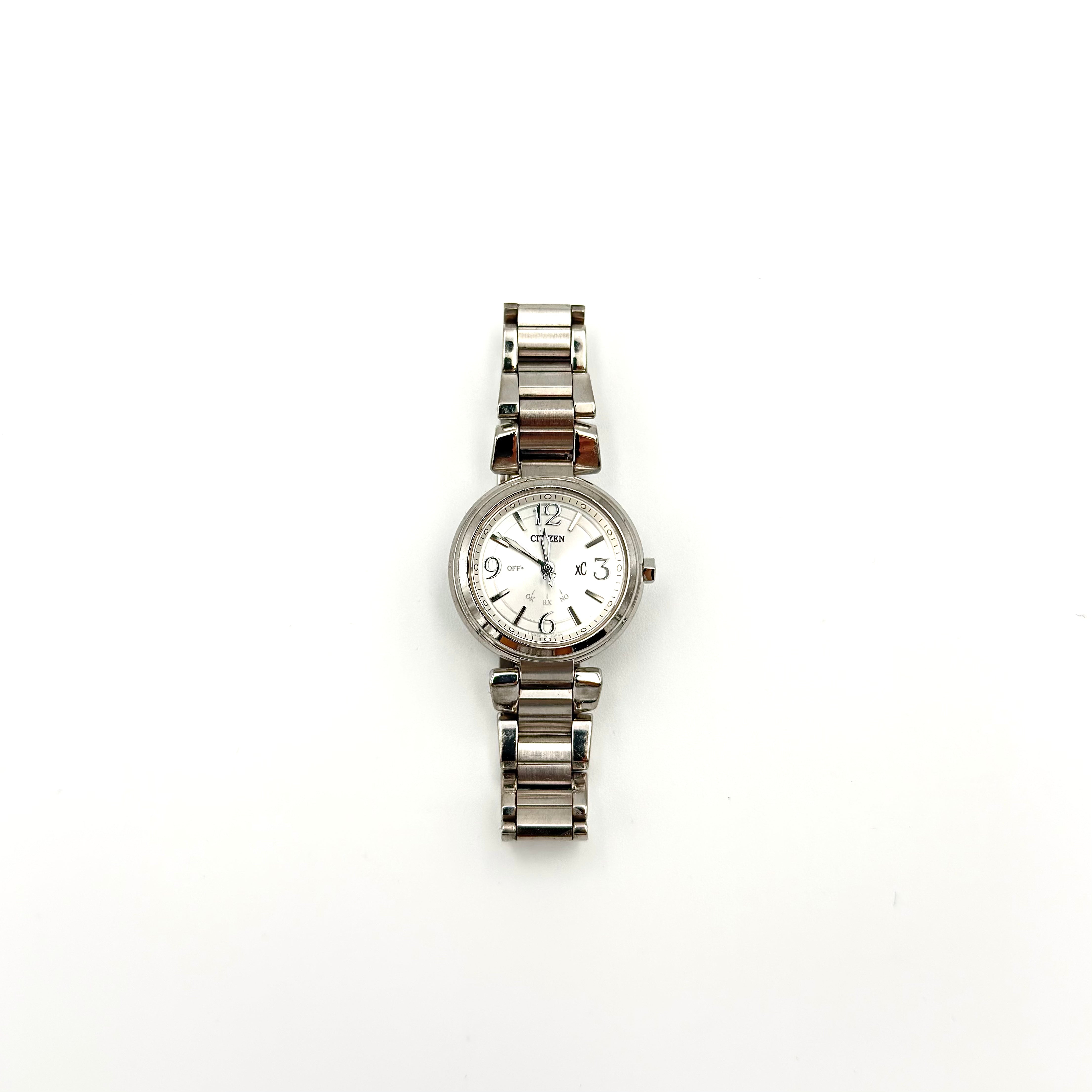 Citizen xC stainless steel watch with white dial, silver-tone hardware, mixed numeral markers, and fold-over clasp.