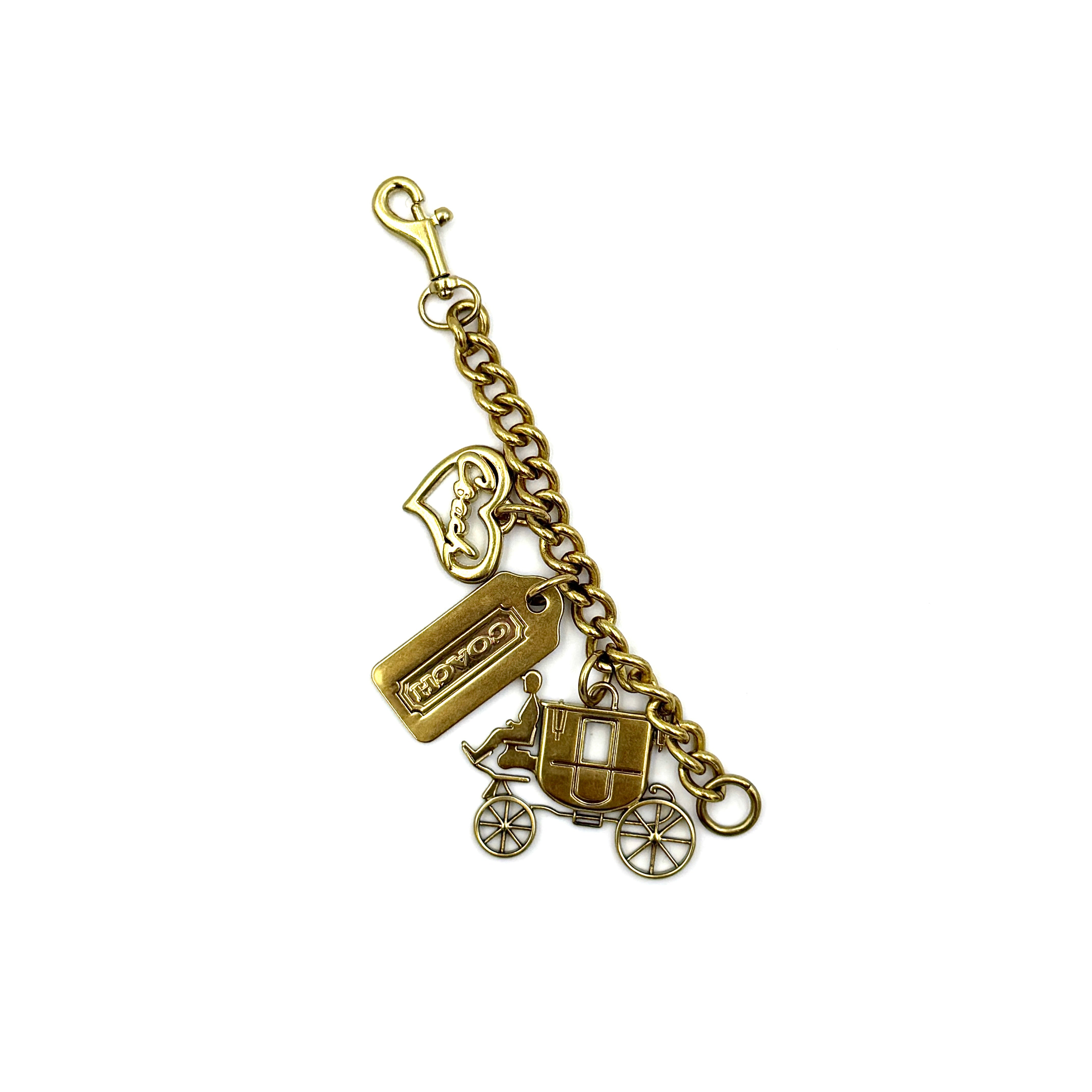 Coach Carriage Heart Tag charm in gold featuring horse and carriage motif, heart tag, and logo detailing.