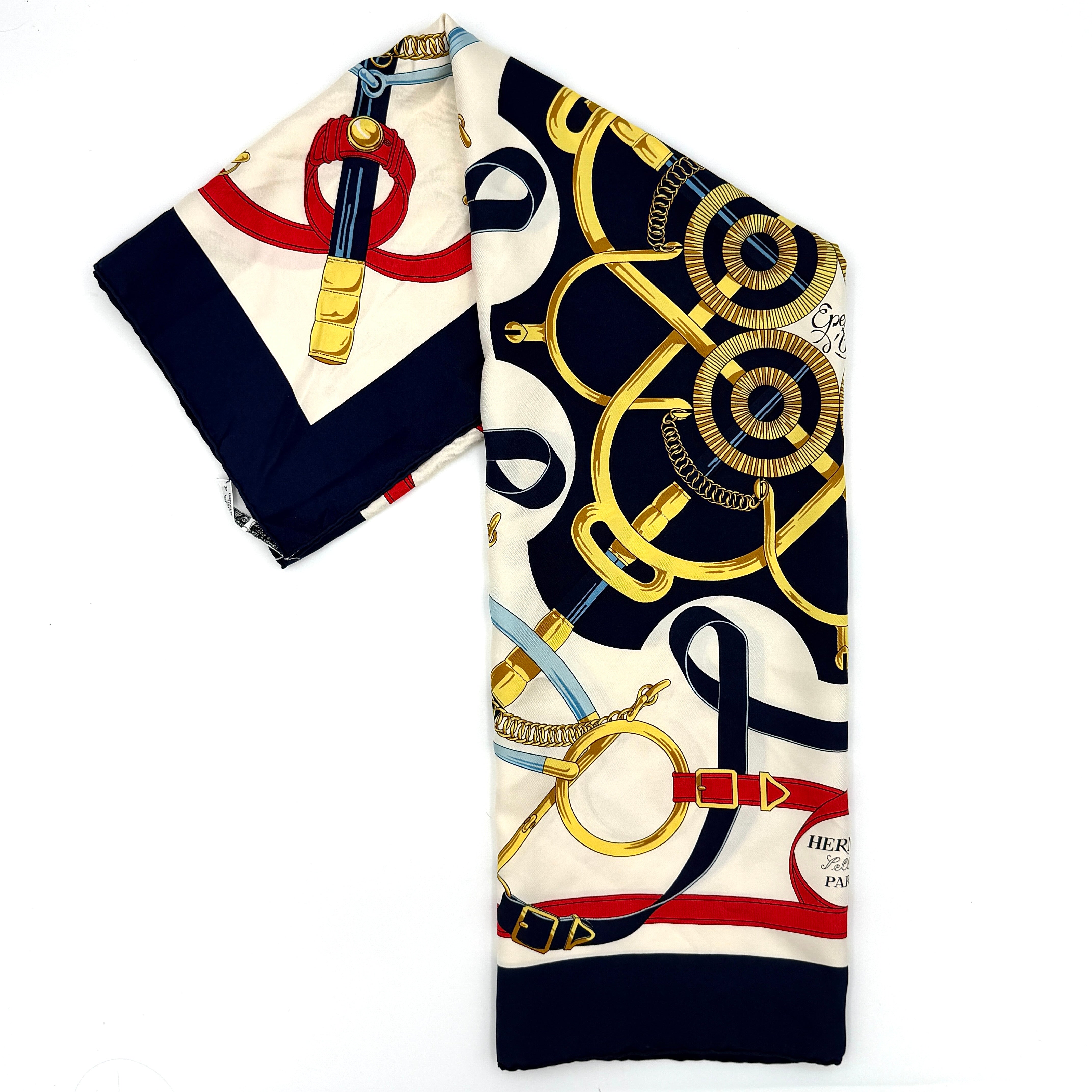 Hermès Éperon d’Or silk scarf featuring multicolor equestrian stirrup motifs in navy, red, gold, and cream.