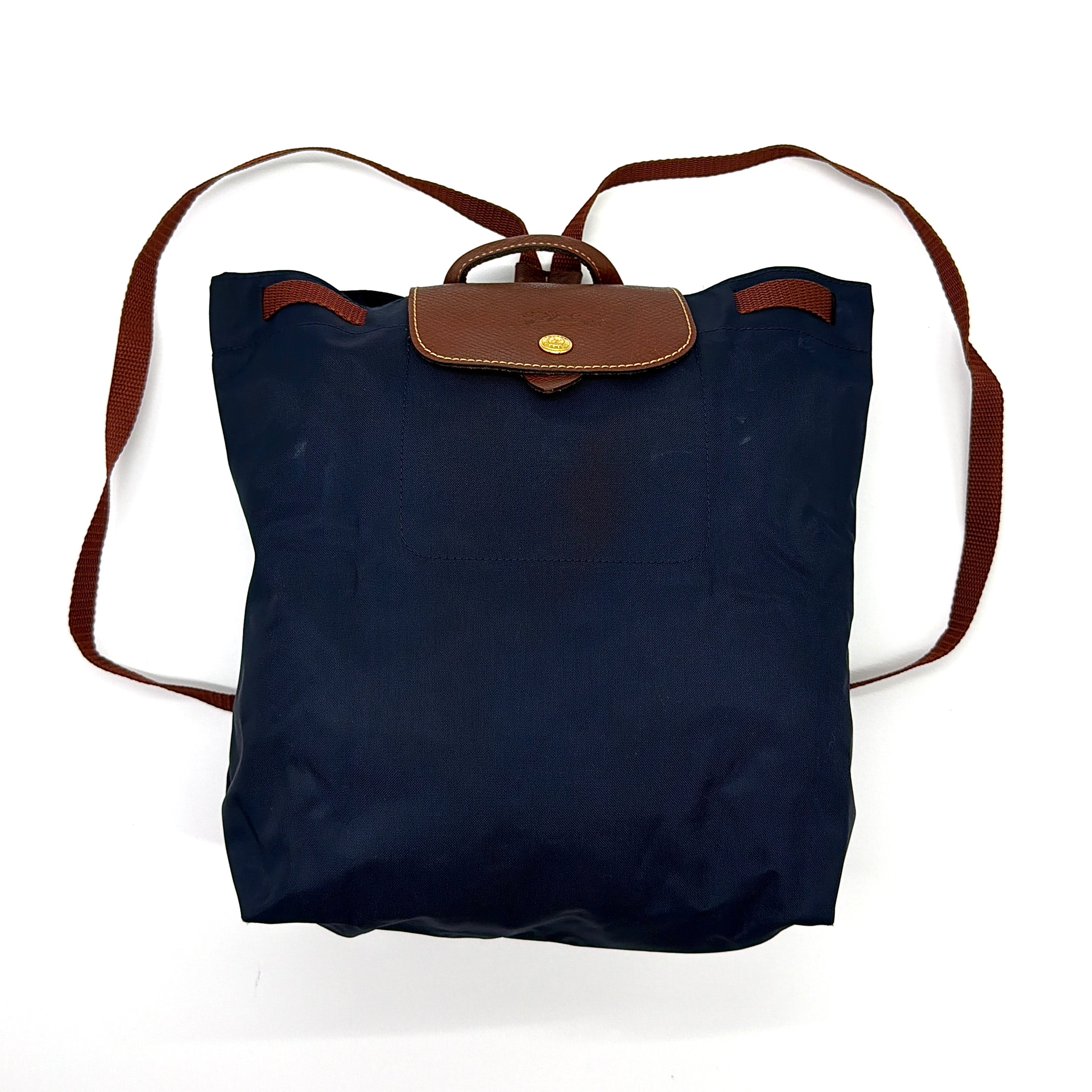 Longchamp Le Pliage Original Backpack in blue nylon with brown leather flap, gold-tone button, and adjustable web straps.