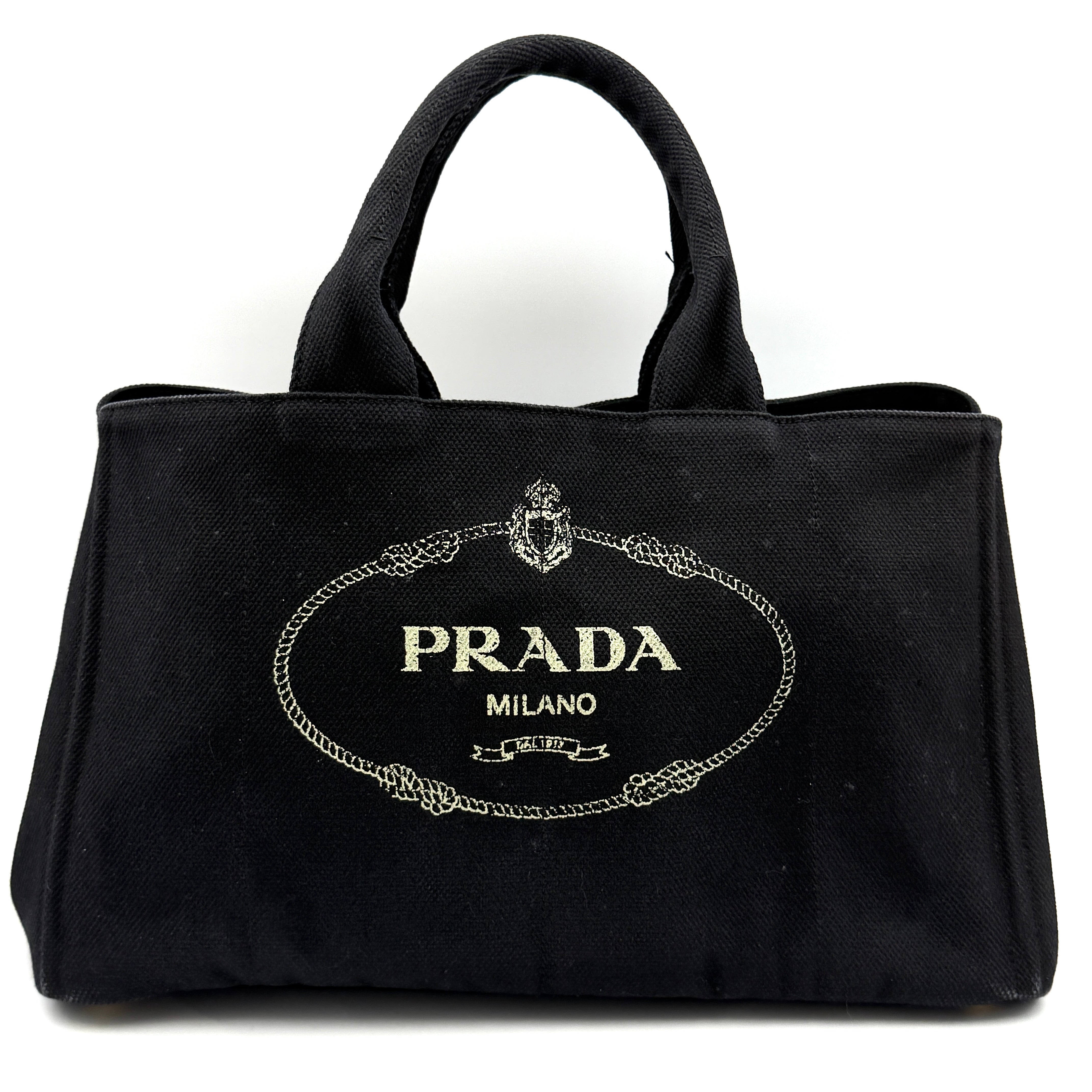 Prada Canapa tote bag in black canvas featuring the iconic Prada Milano logo print and dual top handles.