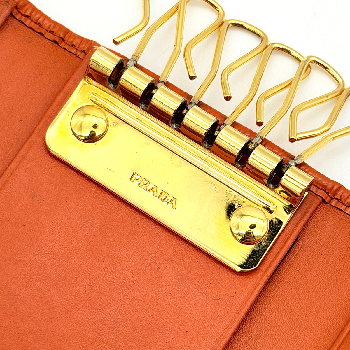 Prada Saffiano leather key case in orange with gold-toned hardware, Prada logo, and authenticity card displayed.