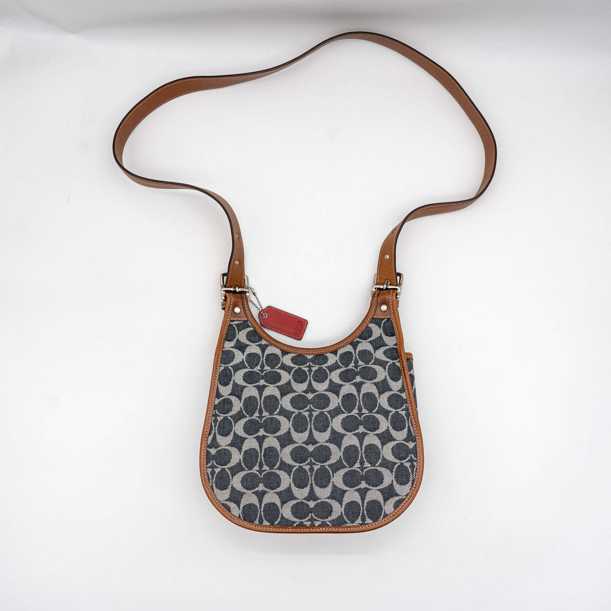 Coach signature denim hobo crossbody bag with red and blue stripe, brown leather trim, and an adjustable strap.