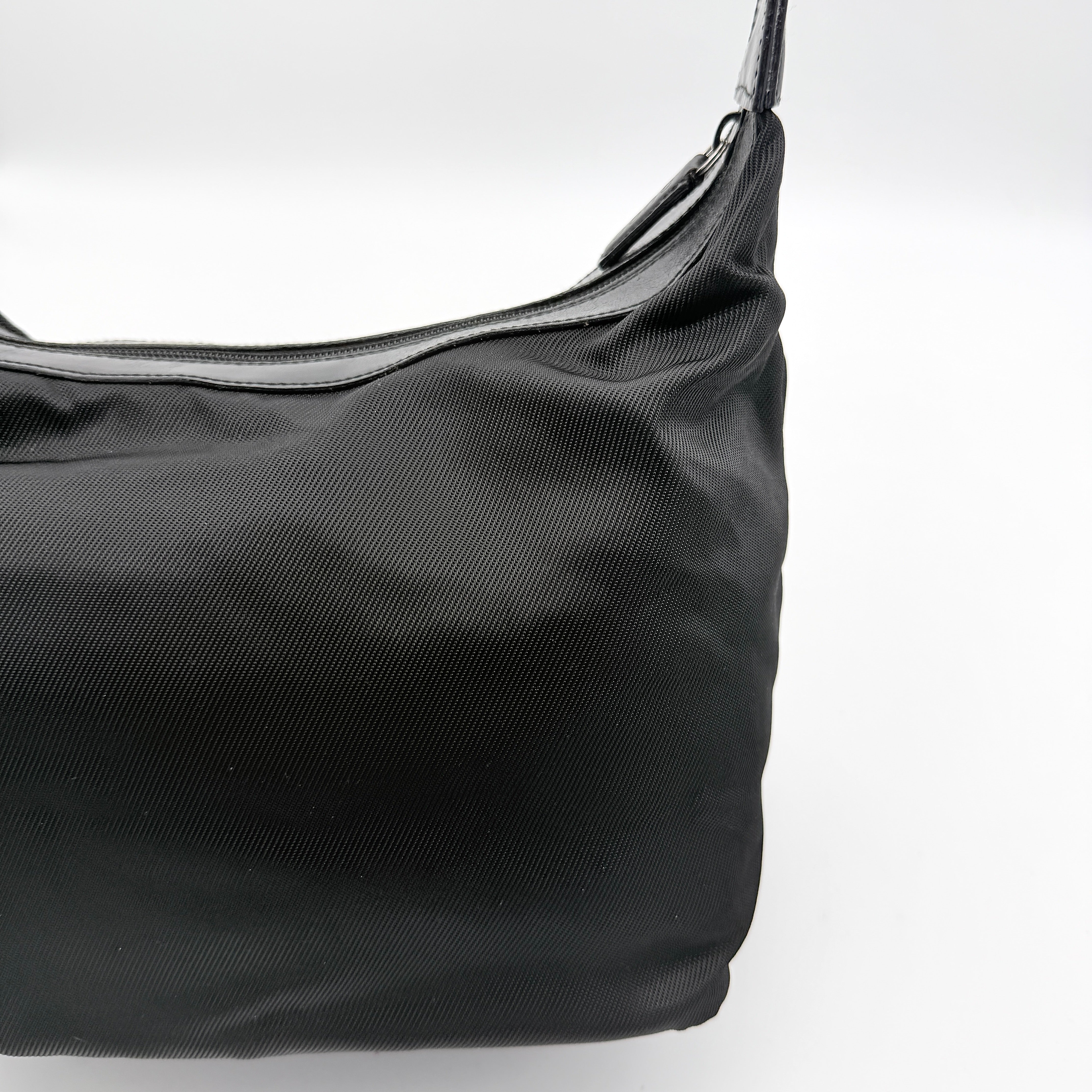 Gucci black nylon shoulder bag with bamboo handle and leather trim, photographed against a white background.