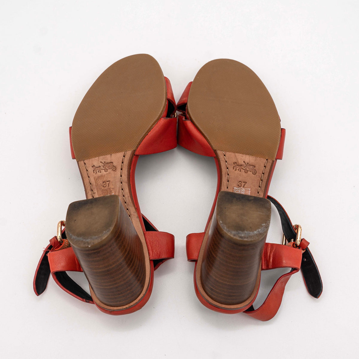 Coach Phoebe block heels in red leather with gold chain detailing, displayed with chunky wood-stacked heels and adjustable ankle straps.