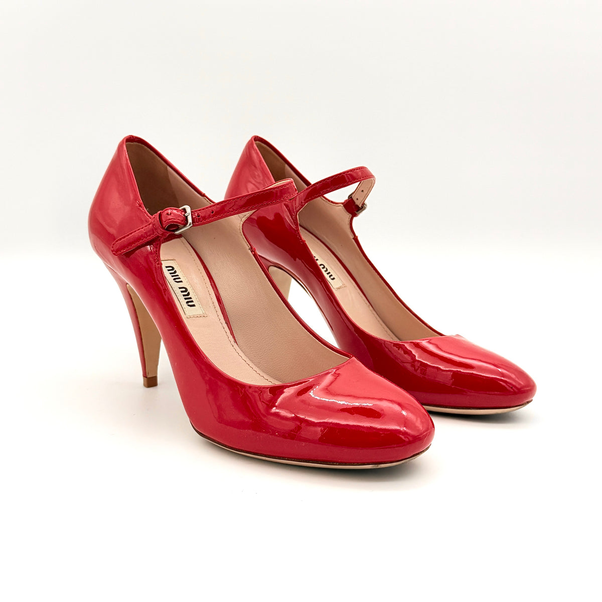 A pair of red patent leather Miu Miu Mary Jane heels with adjustable buckle straps and high heels, displayed against a white background.