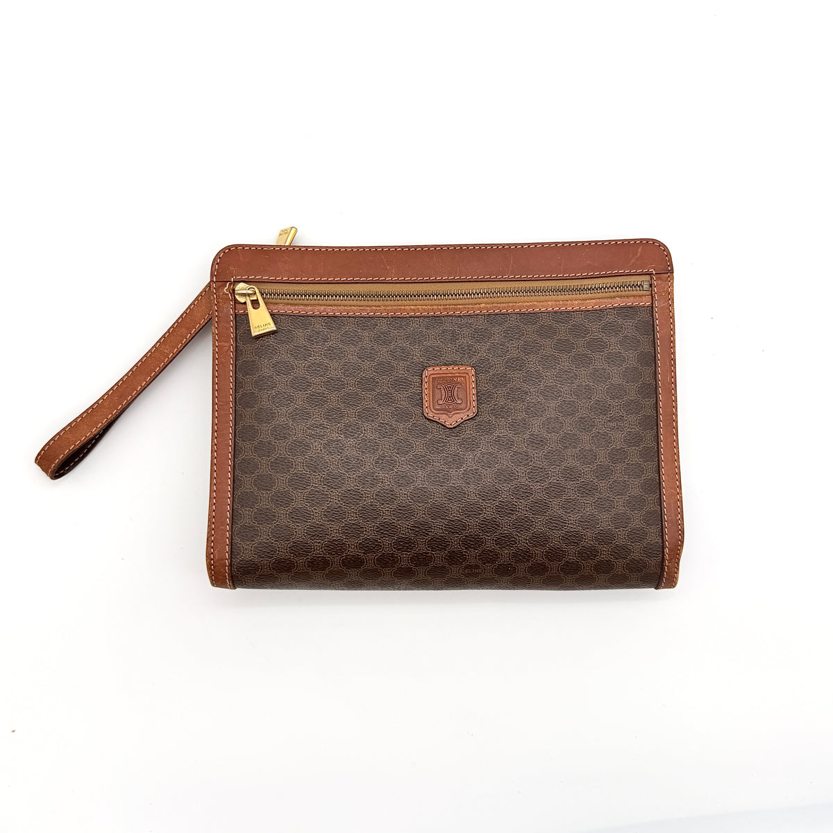Celine Triomphe Macadam clutch bag in brown canvas with tan leather trim and gold hardware, shown with wrist strap.