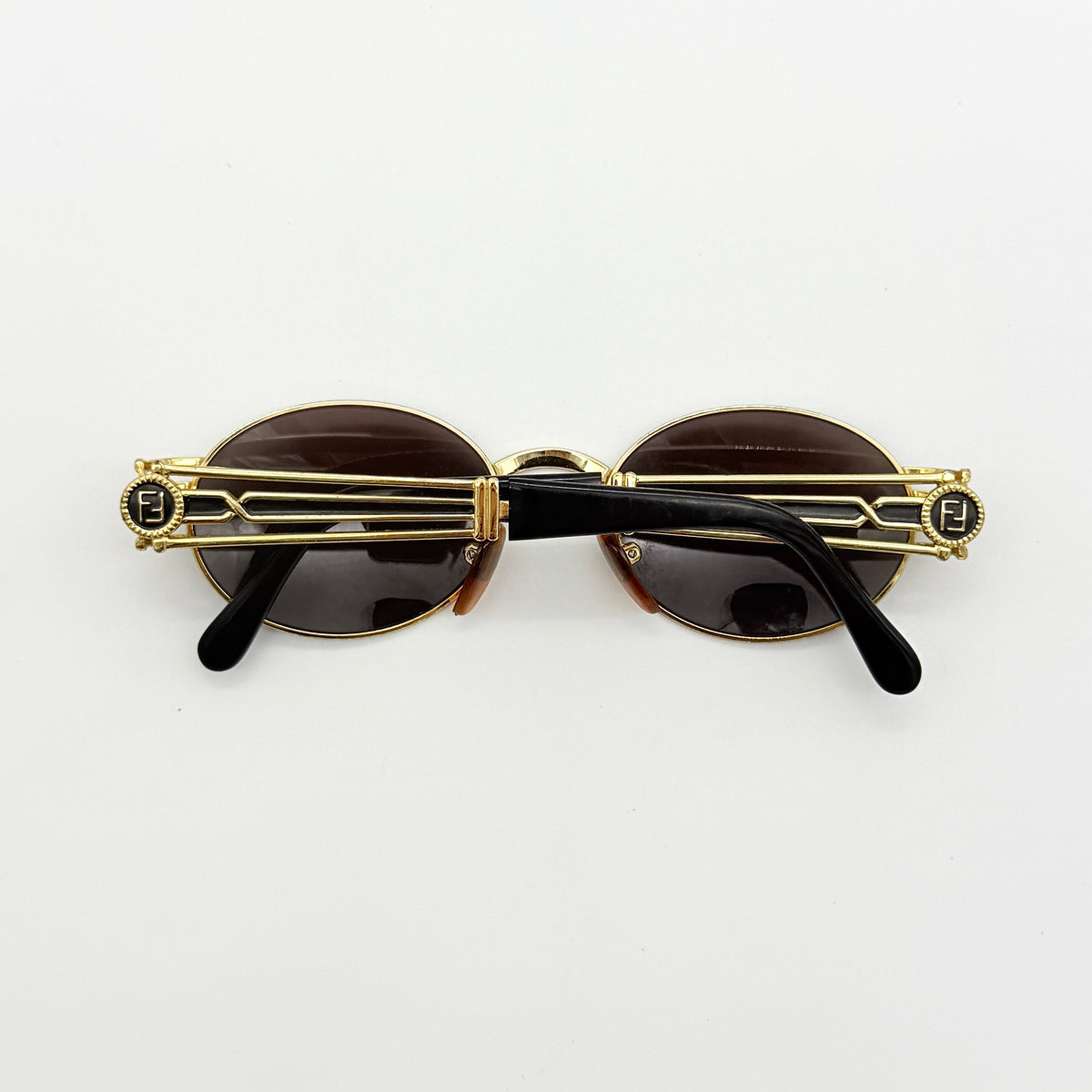 Fendi FF SL7031 oval sunglasses with gold-tone frame, brown lenses, and black arms, shown at an angled side view.
