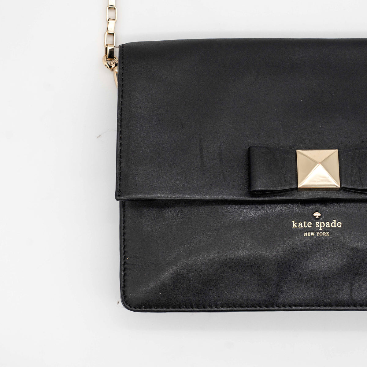 Kate Spade New York black leather shoulder bag with gold chain strap and bow detail, displayed against a white background.