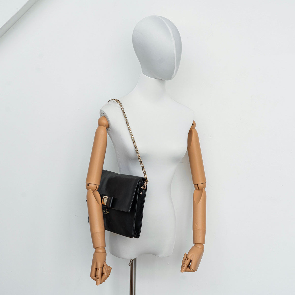 Kate Spade New York black leather shoulder bag with gold chain strap and bow detail, displayed against a white background.