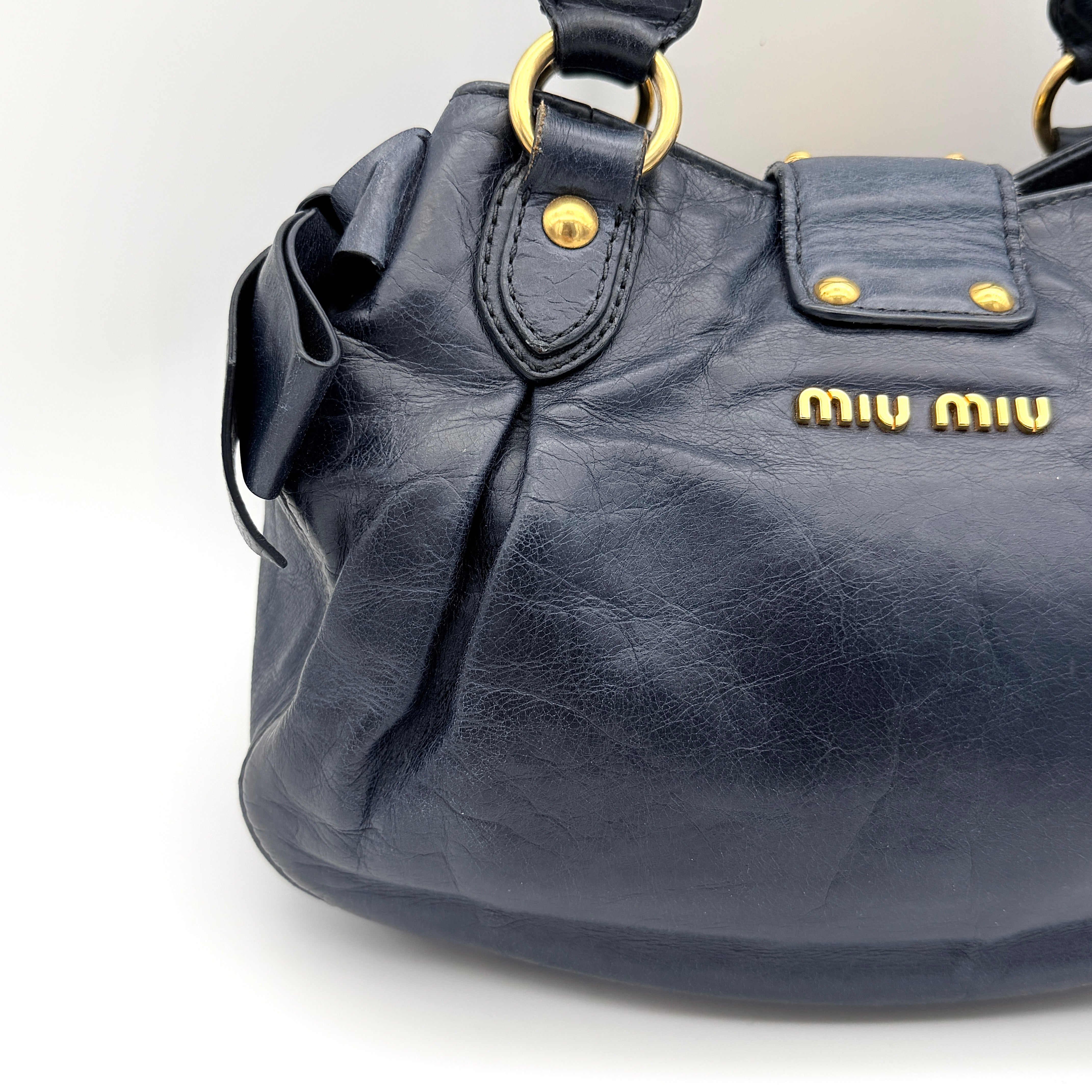Miu Miu navy blue Vitello Lux Bow Satchel with gold-tone hardware, detachable strap, and dust bag.