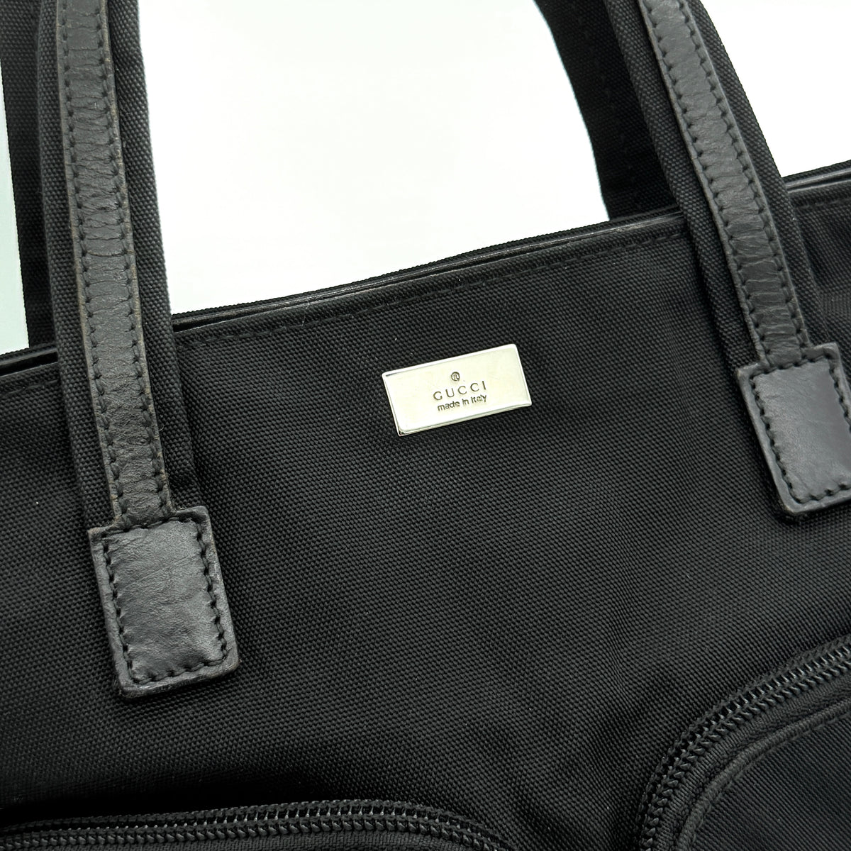 Front view of the Gucci black nylon tote with dual zip pockets and leather top handles.