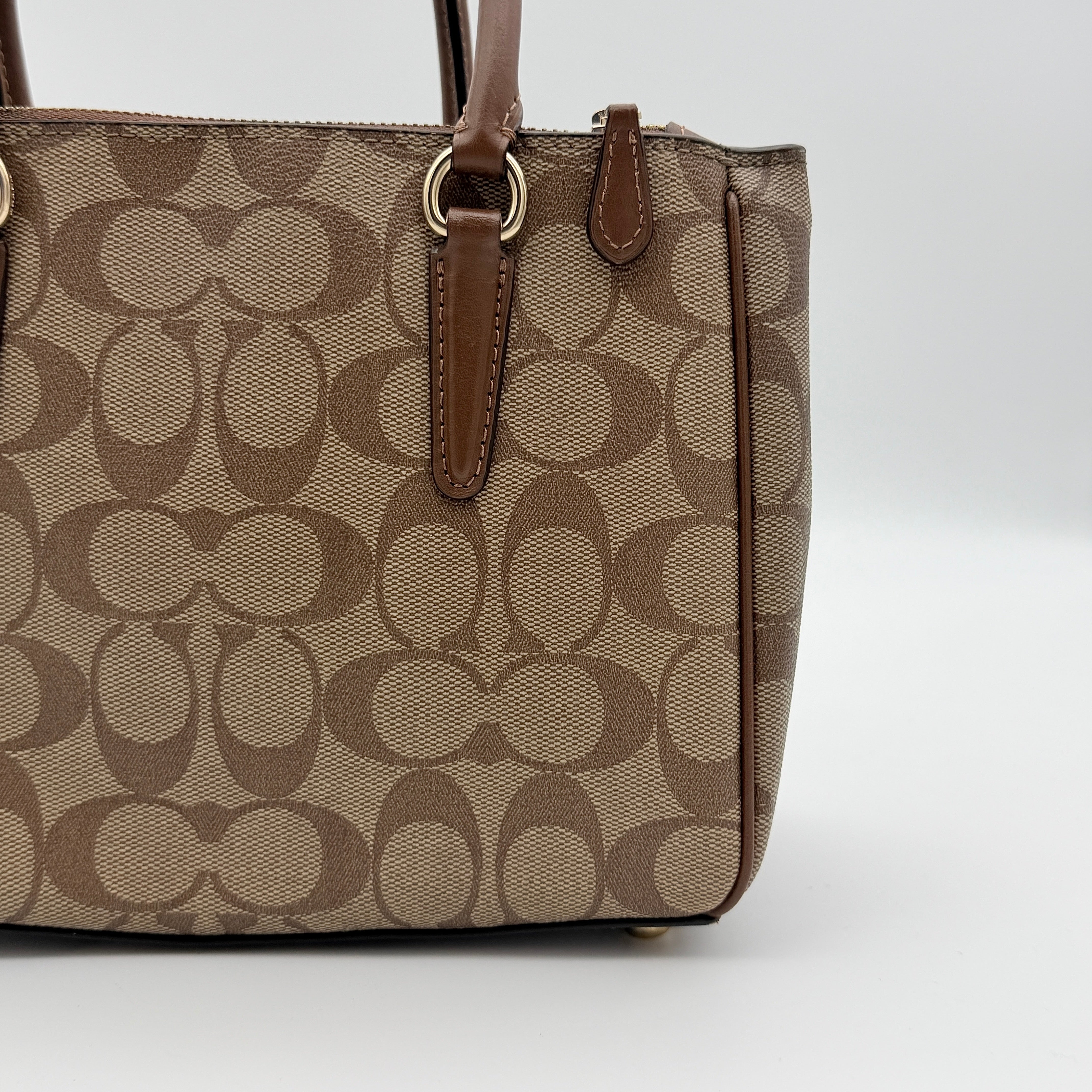 Coach Christie Carryall in beige and brown canvas with gold hardware and detachable strap, photographed in a studio setting.