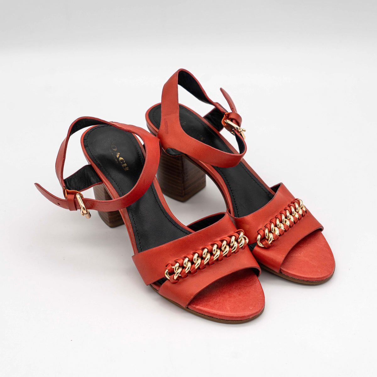 Coach Phoebe block heels in red leather with gold chain detailing, displayed with chunky wood-stacked heels and adjustable ankle straps.