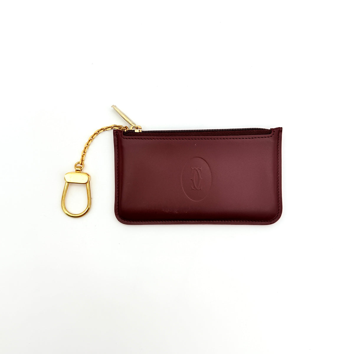 Cartier Must de Cartier burgundy leather coin purse with gold chain key holder and embossed logo, photographed on white.
