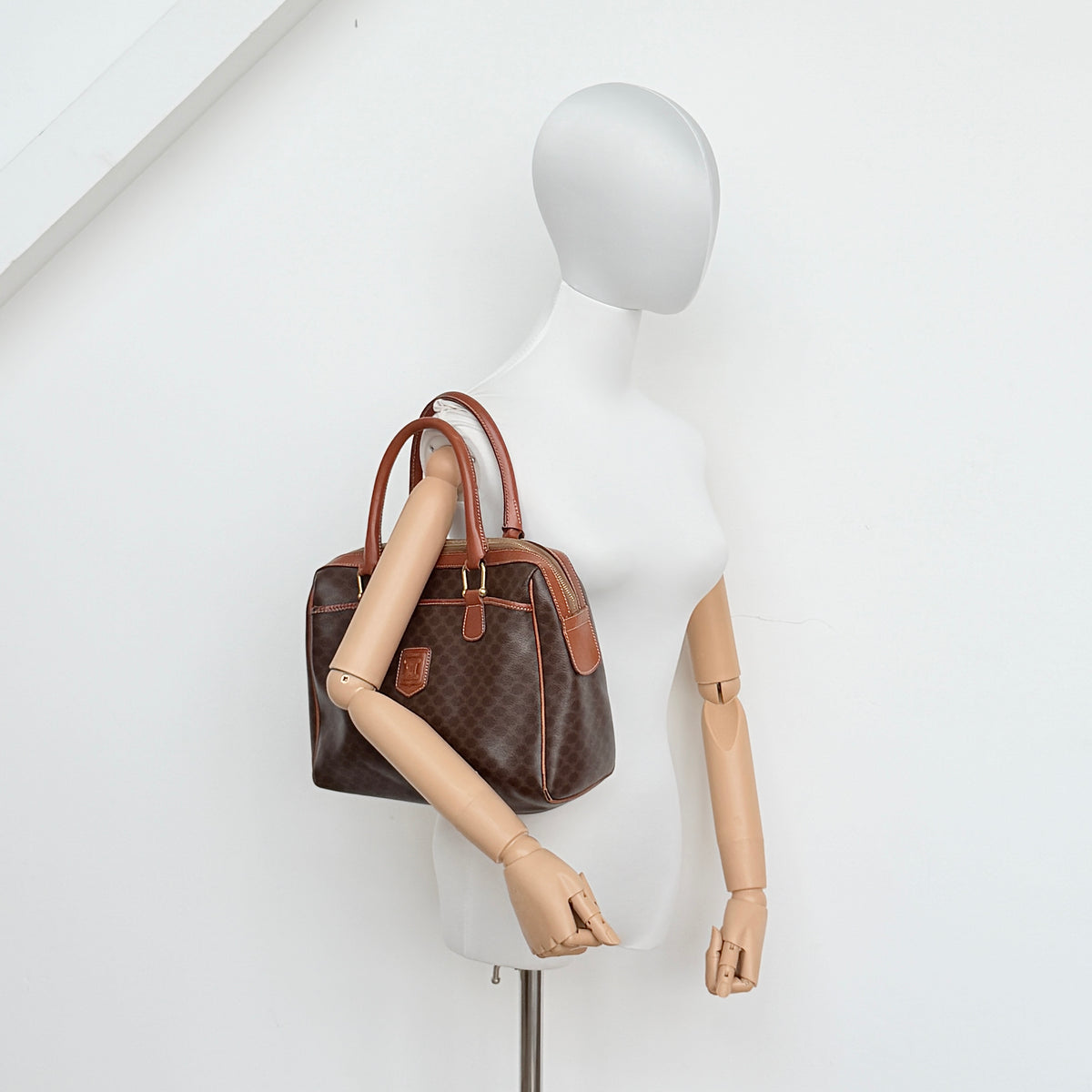 Celine Triomphe Macadam Boston Bag in brown coated canvas with tan leather handles and gold hardware on a white background.