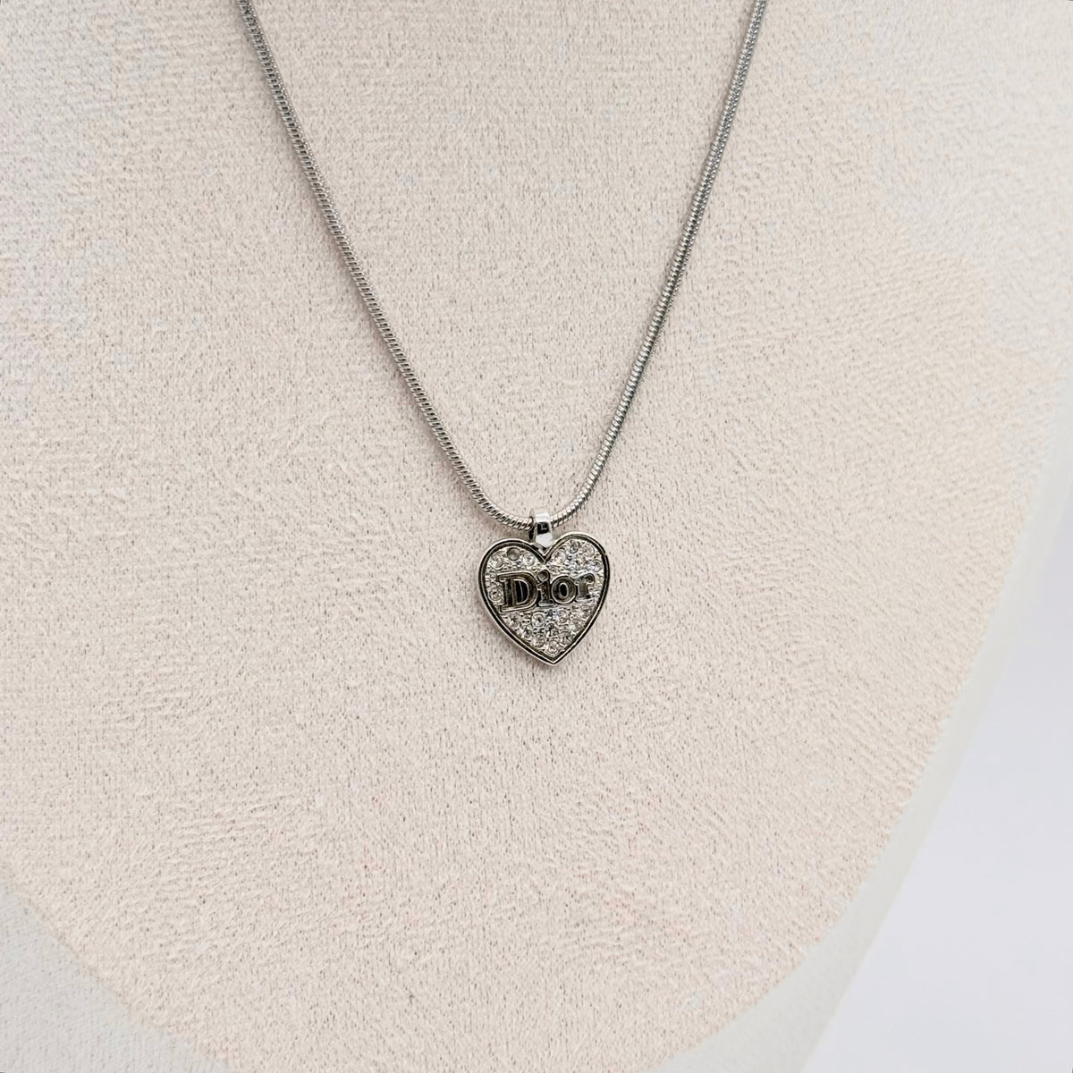 Dior silver necklace with a rhinestone heart pendant and Dior logo, laid flat with CD tag visible.