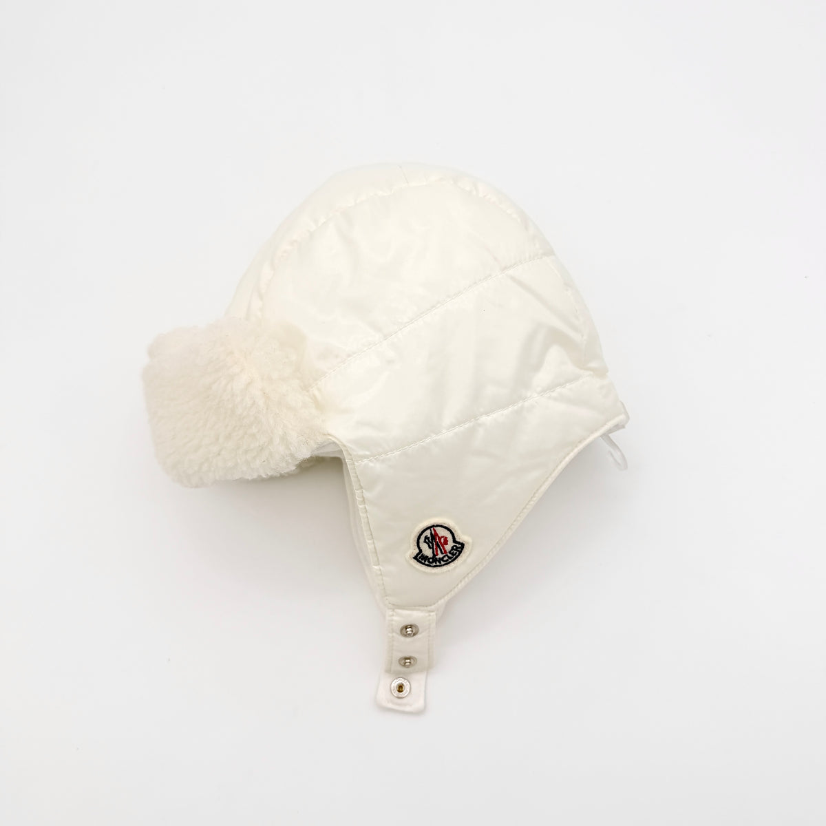 Moncler ivory quilted trapper hat with plush faux fur trim and signature logo patch displayed on white background.