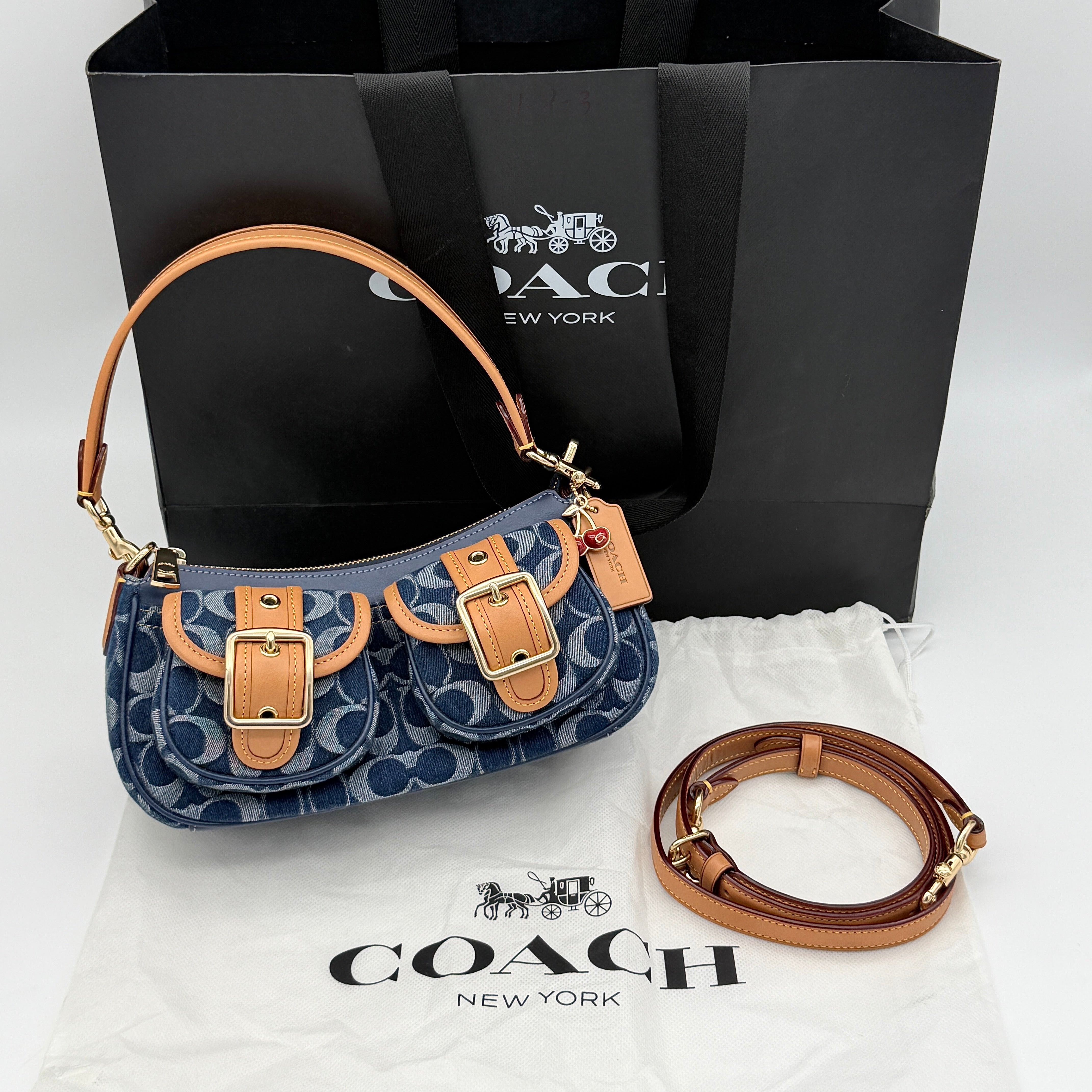 Coach Signature Ashton shoulder bag in blue denim and tan leather with gold hardware, shown with removable strap and dust bag.