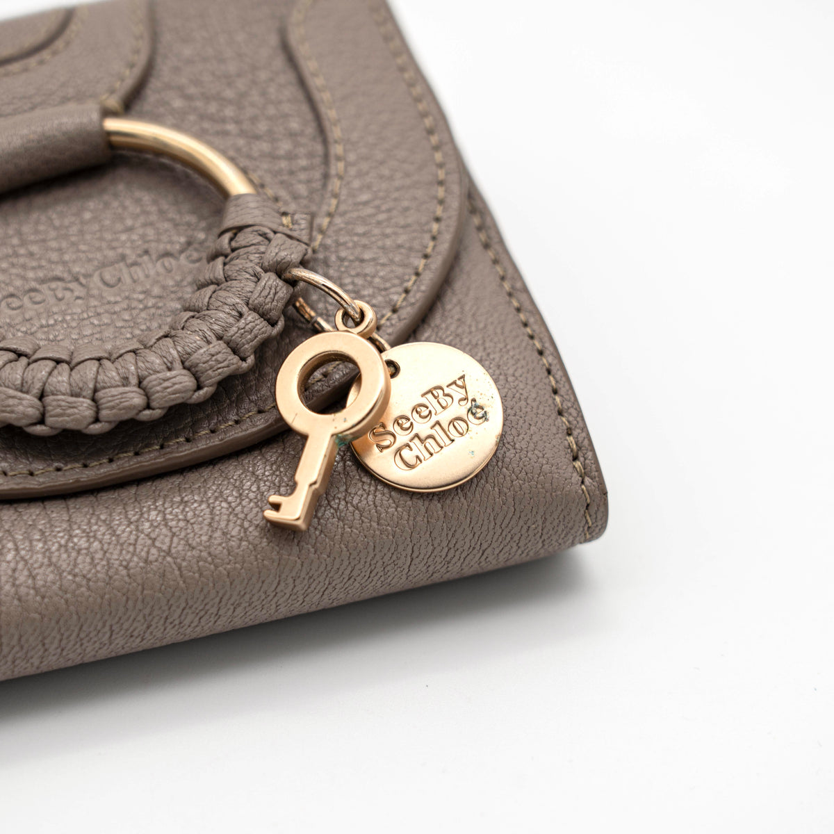 See by Chloe Hana tri-fold wallet in grey grained leather with gold-tone ring and charms, photographed closed on a white background.