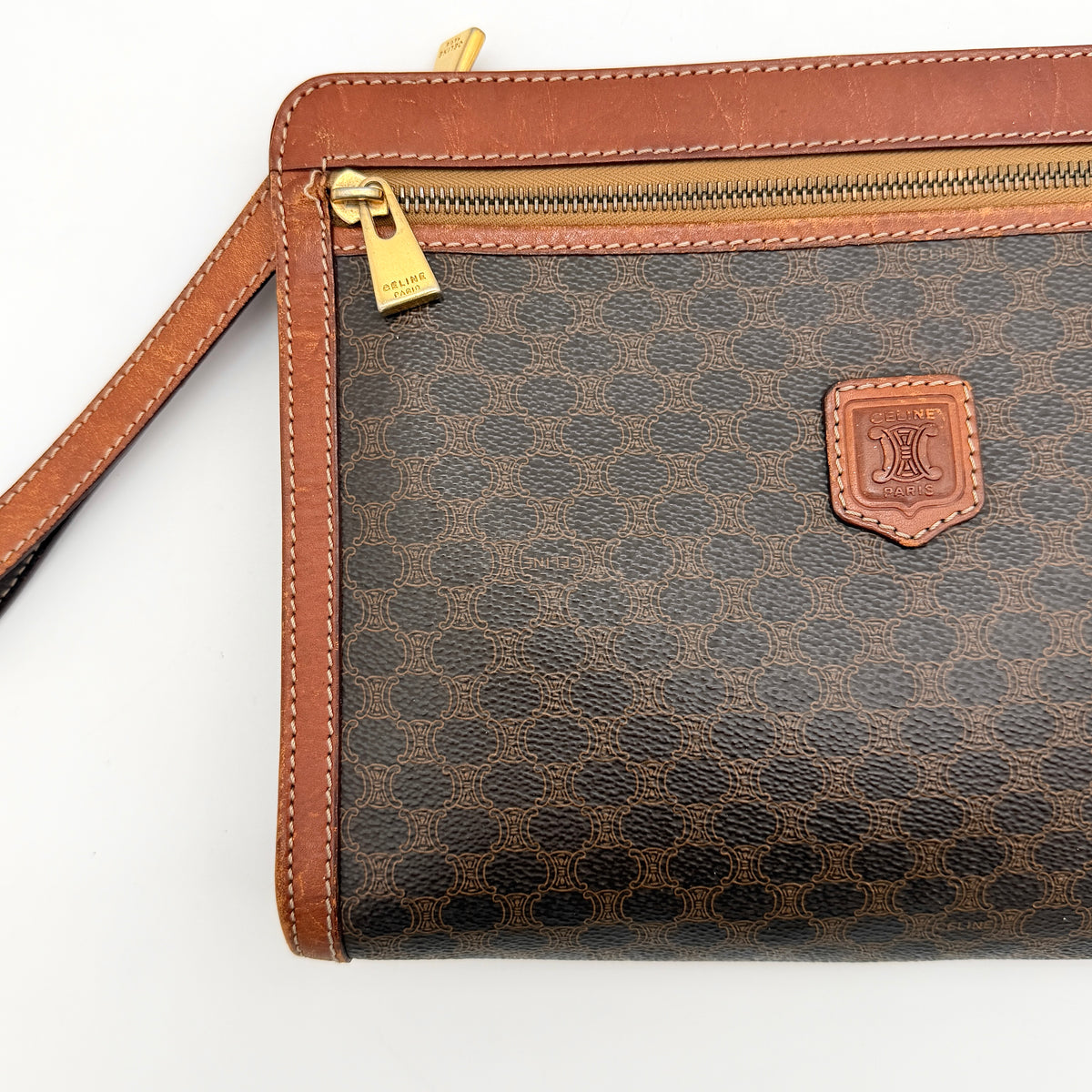 Celine Triomphe Macadam clutch bag in brown canvas with tan leather trim and gold hardware, shown with wrist strap.