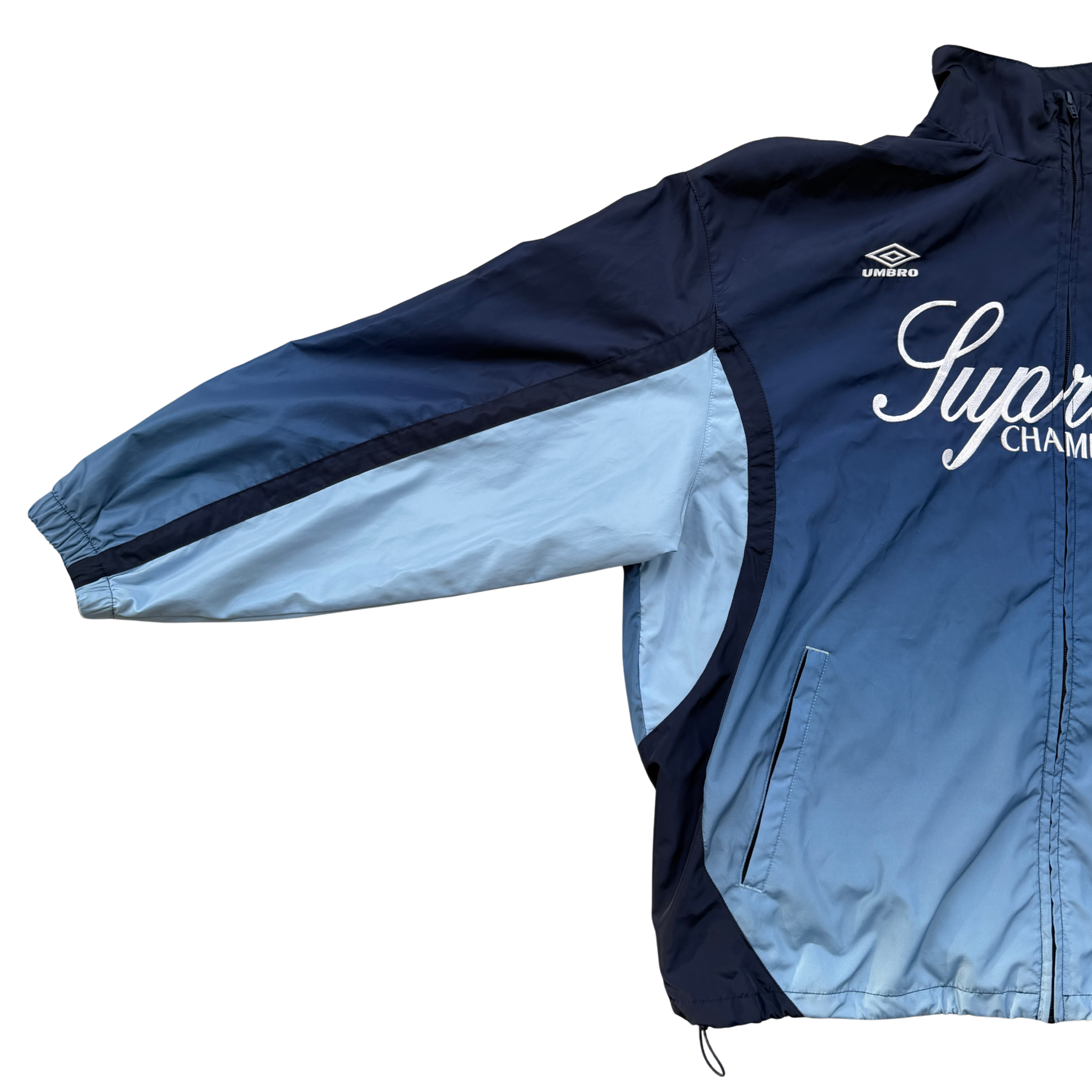 Supreme x Umbro blue gradient track jacket with white Supreme Champions lettering and crest, shown zipped with elastic cuffs and hem.