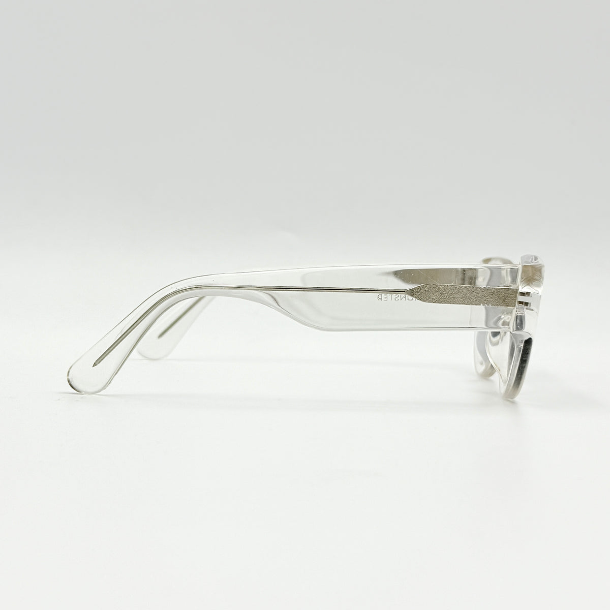 Gentle Monster Tazi transparent sunglasses with grey lenses and clear acetate frame, softly styled alongside the branded case.