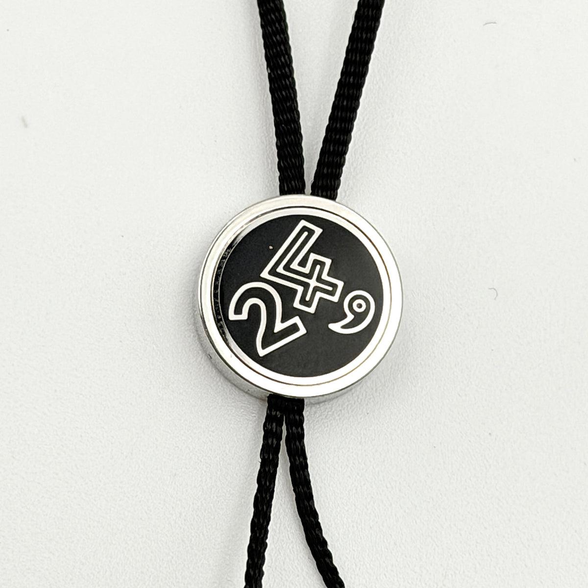 Hermès black cord cell phone charm strap with round silver-tone graphic accent, shown against a white background.