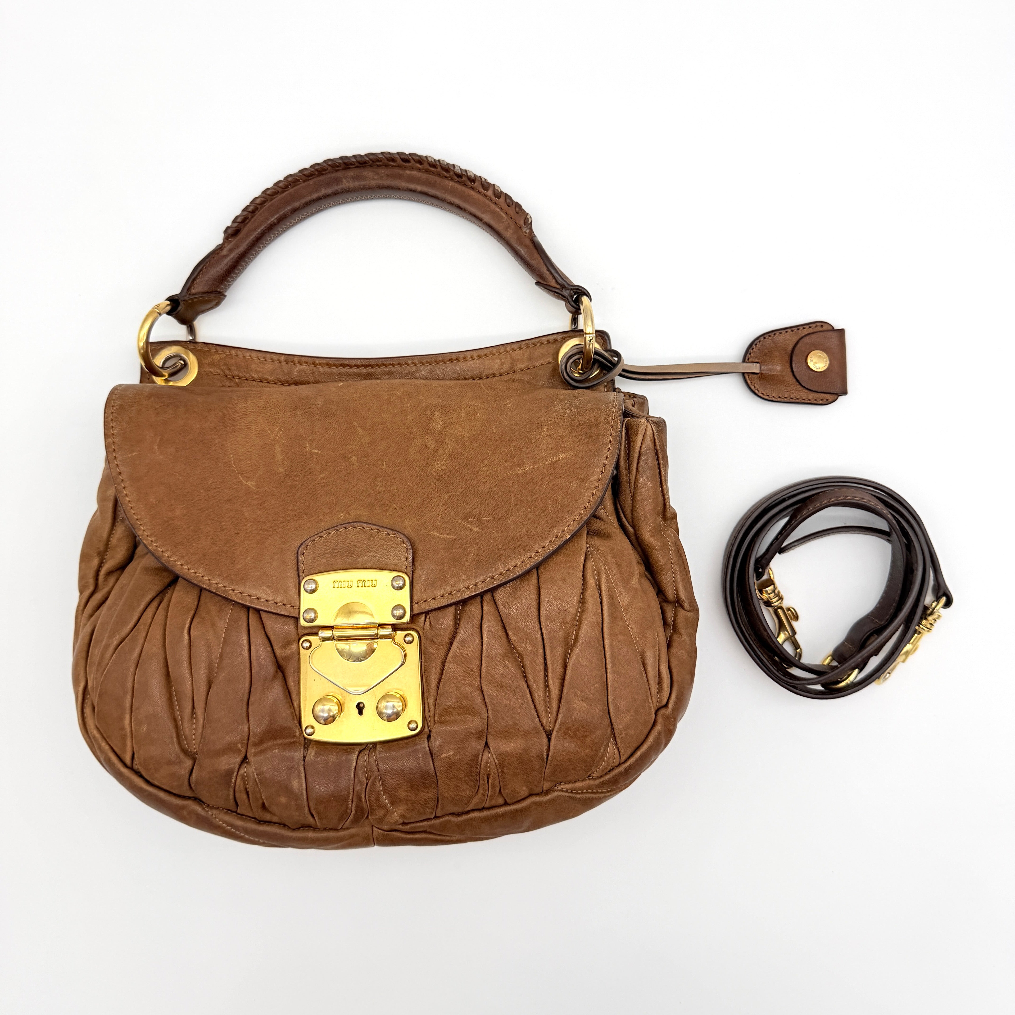 Miu Miu brown Matelasse Coffer Hobo bag with gold hardware, detachable strap, and dust bag displayed on a flat surface.