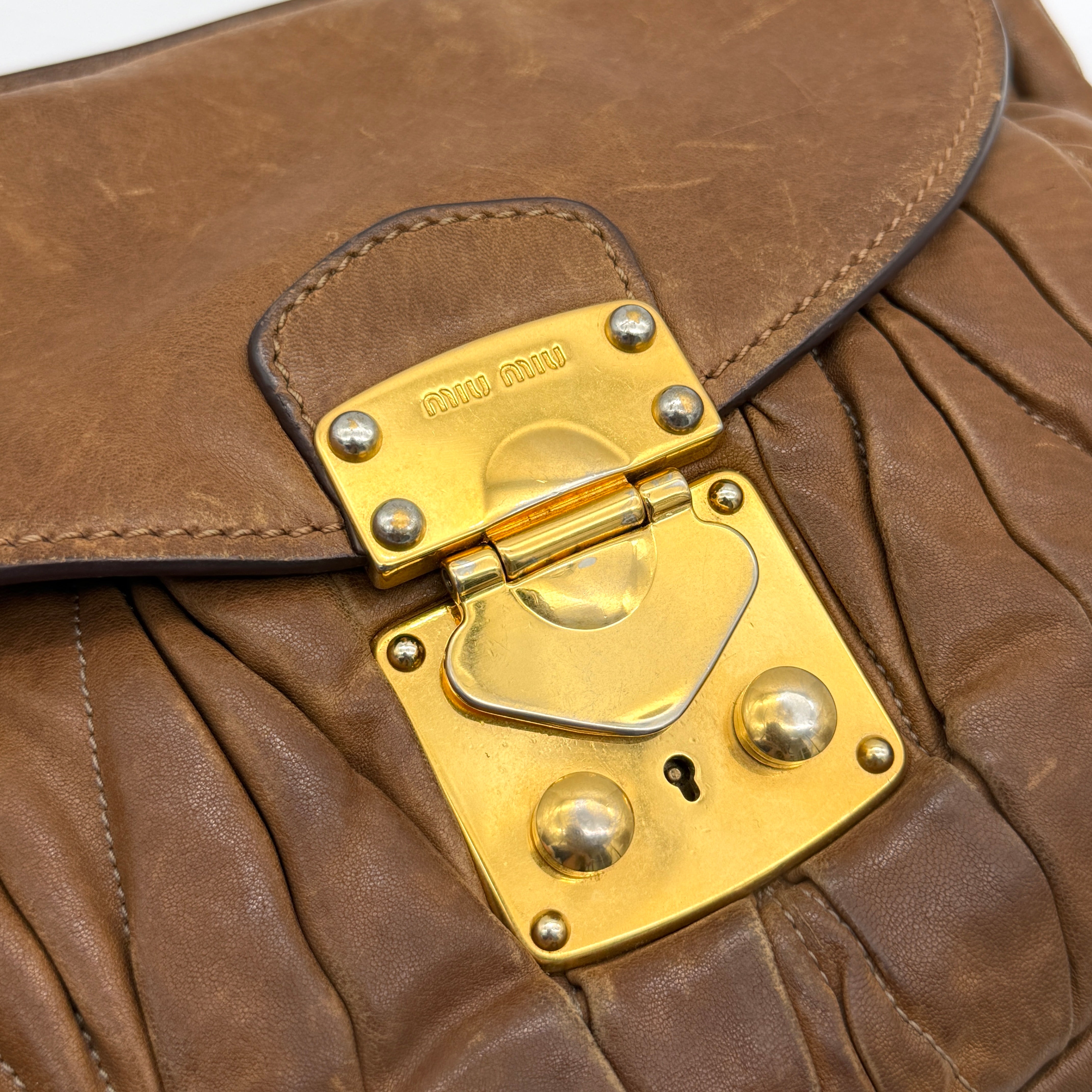 Miu Miu brown Matelasse Coffer Hobo bag with gold hardware, detachable strap, and dust bag displayed on a flat surface.