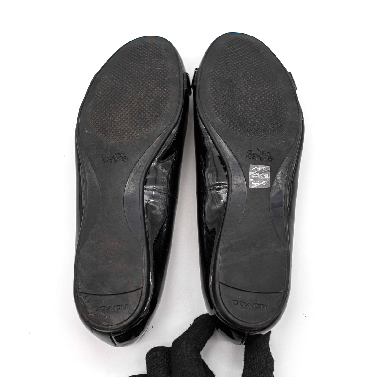Coach Oswald Turnlock black patent leather ballet flats with dark metal hardware on the toe, photographed on a white background.