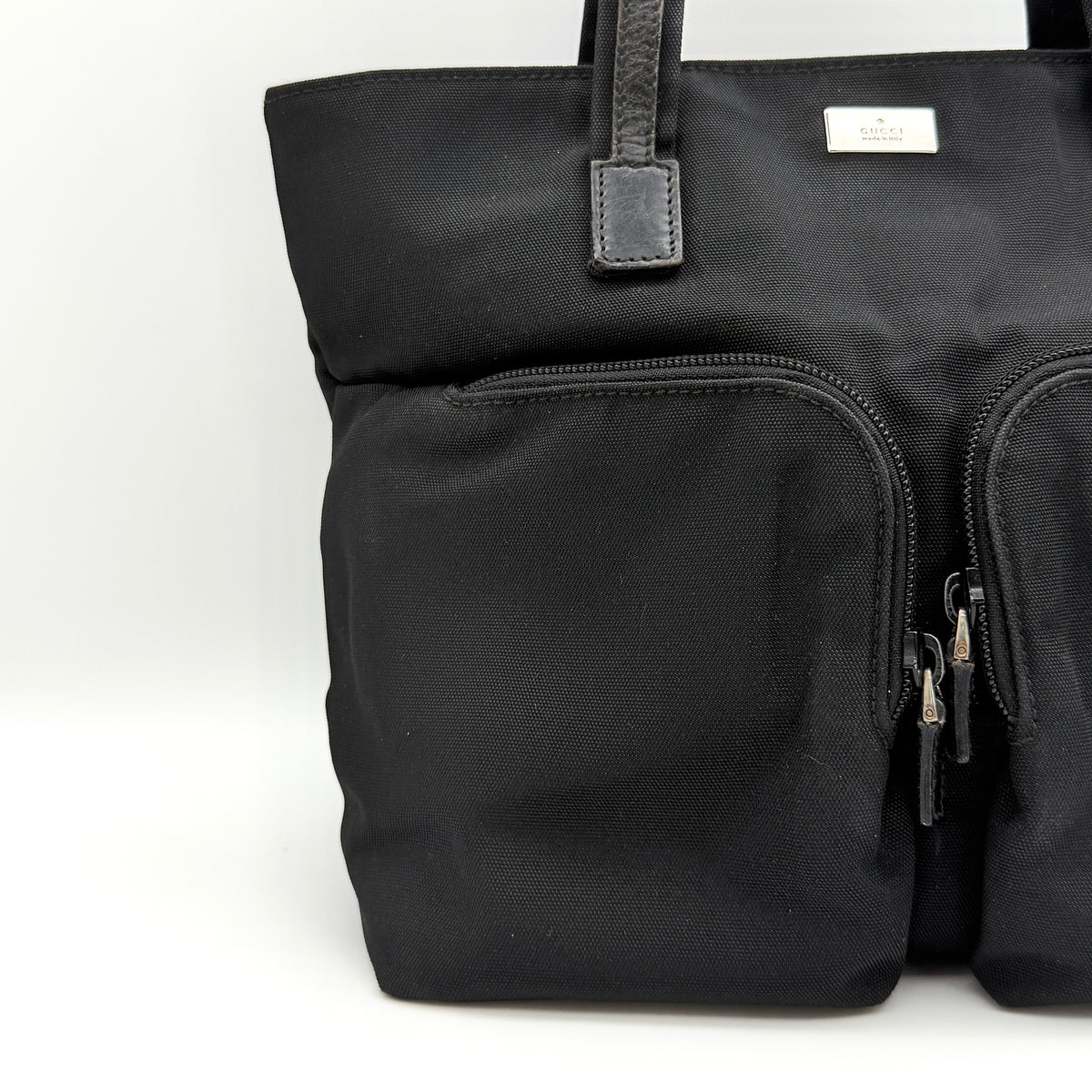 Front view of the Gucci black nylon tote with dual zip pockets and leather top handles.