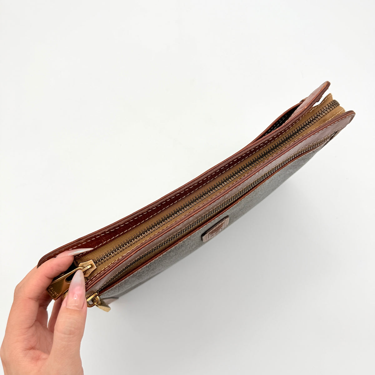 Celine Triomphe Macadam clutch bag in brown canvas with tan leather trim and gold hardware, shown with wrist strap.