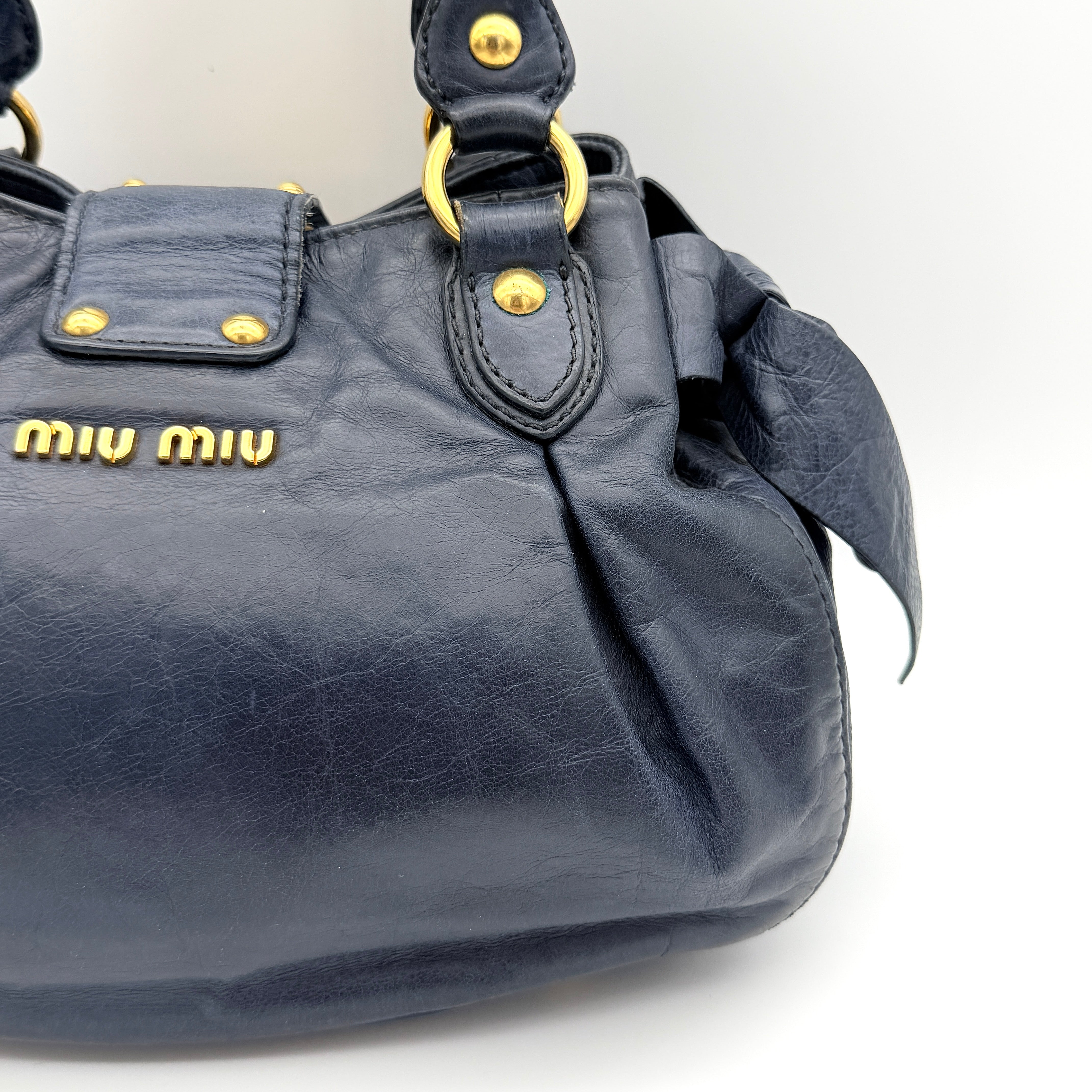 Miu Miu navy blue Vitello Lux Bow Satchel with gold-tone hardware, detachable strap, and dust bag.
