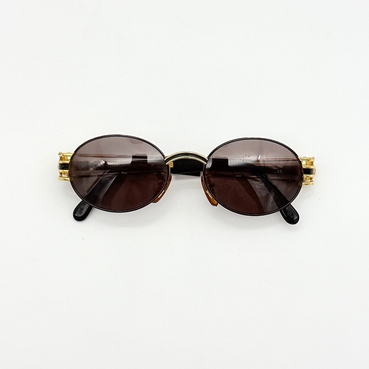 Fendi FF SL7031 oval sunglasses with gold-tone frame, brown lenses, and black arms, shown at an angled side view.