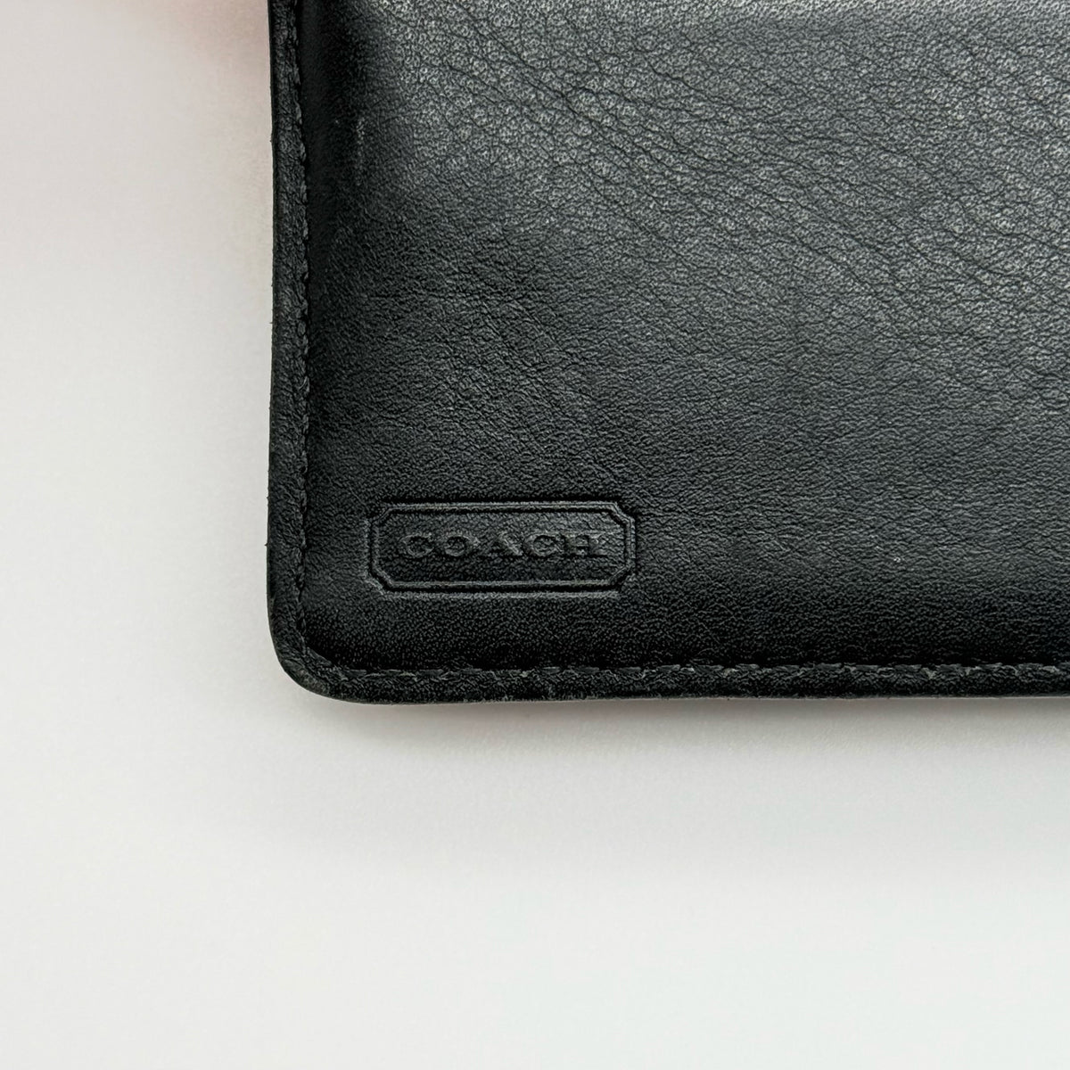 Coach black Soho Bifold Wallet with signature silver buckle and contrast stitching, shown closed against a white background.