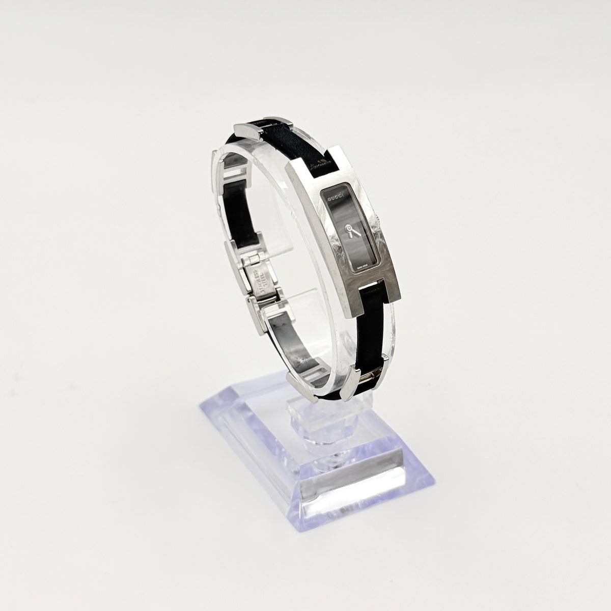 Gucci 3900L black dial watch with silver-tone rectangular case and black leather strap displayed on a stand