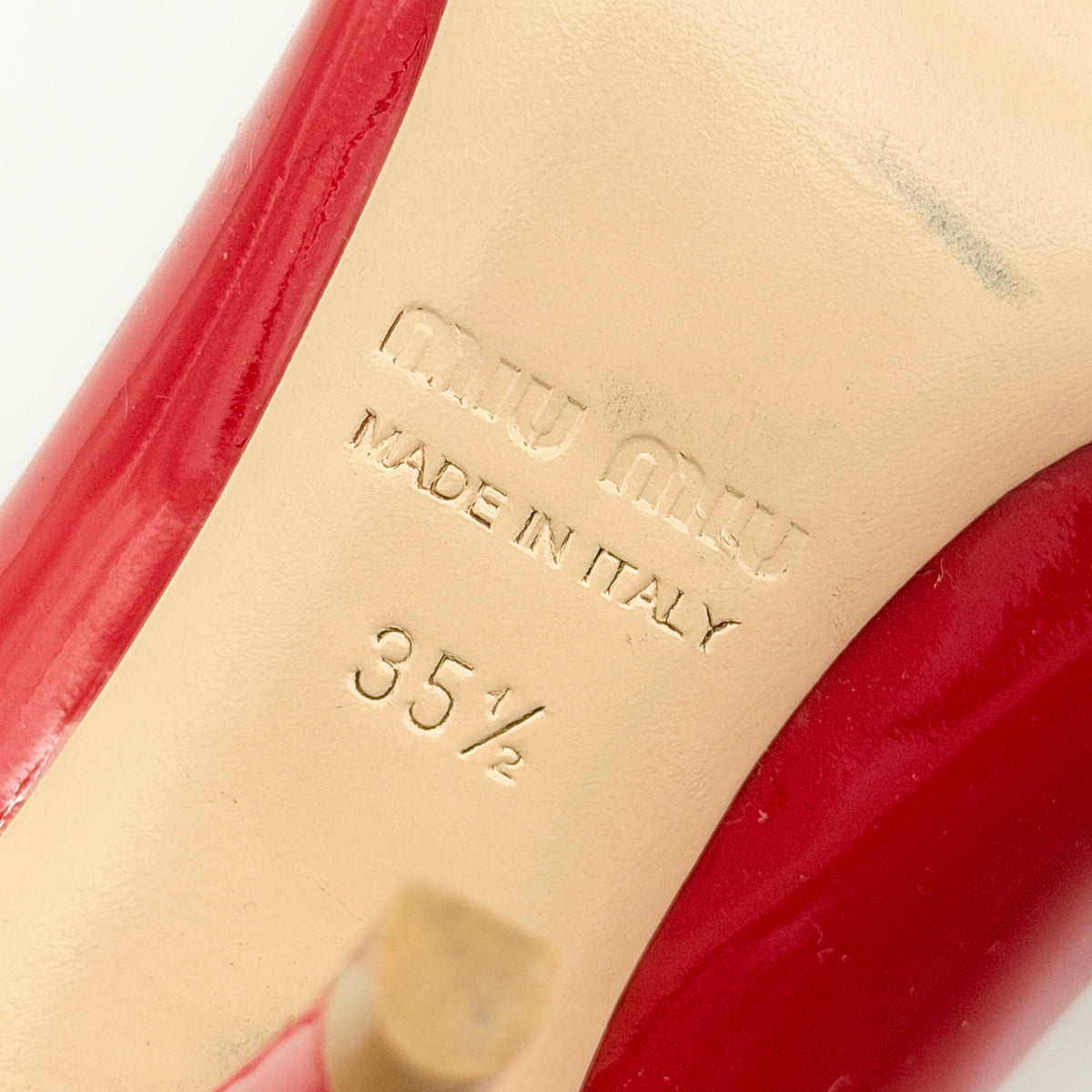 A pair of red patent leather Miu Miu Mary Jane heels with adjustable buckle straps and high heels, displayed against a white background.
