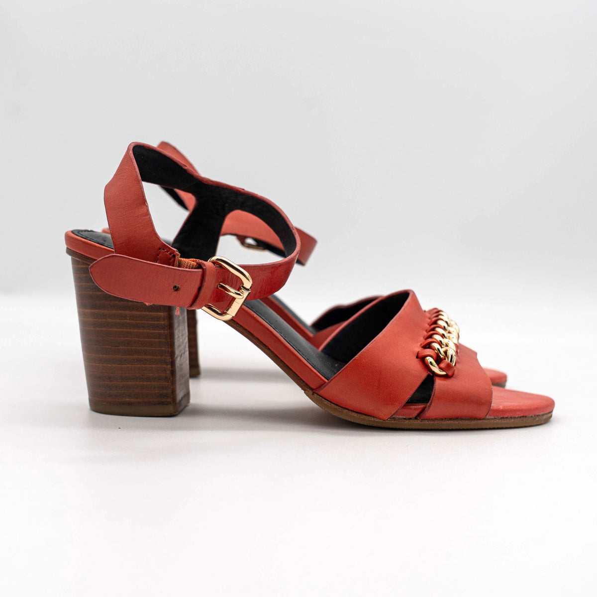 Coach Phoebe block heels in red leather with gold chain detailing, displayed with chunky wood-stacked heels and adjustable ankle straps.