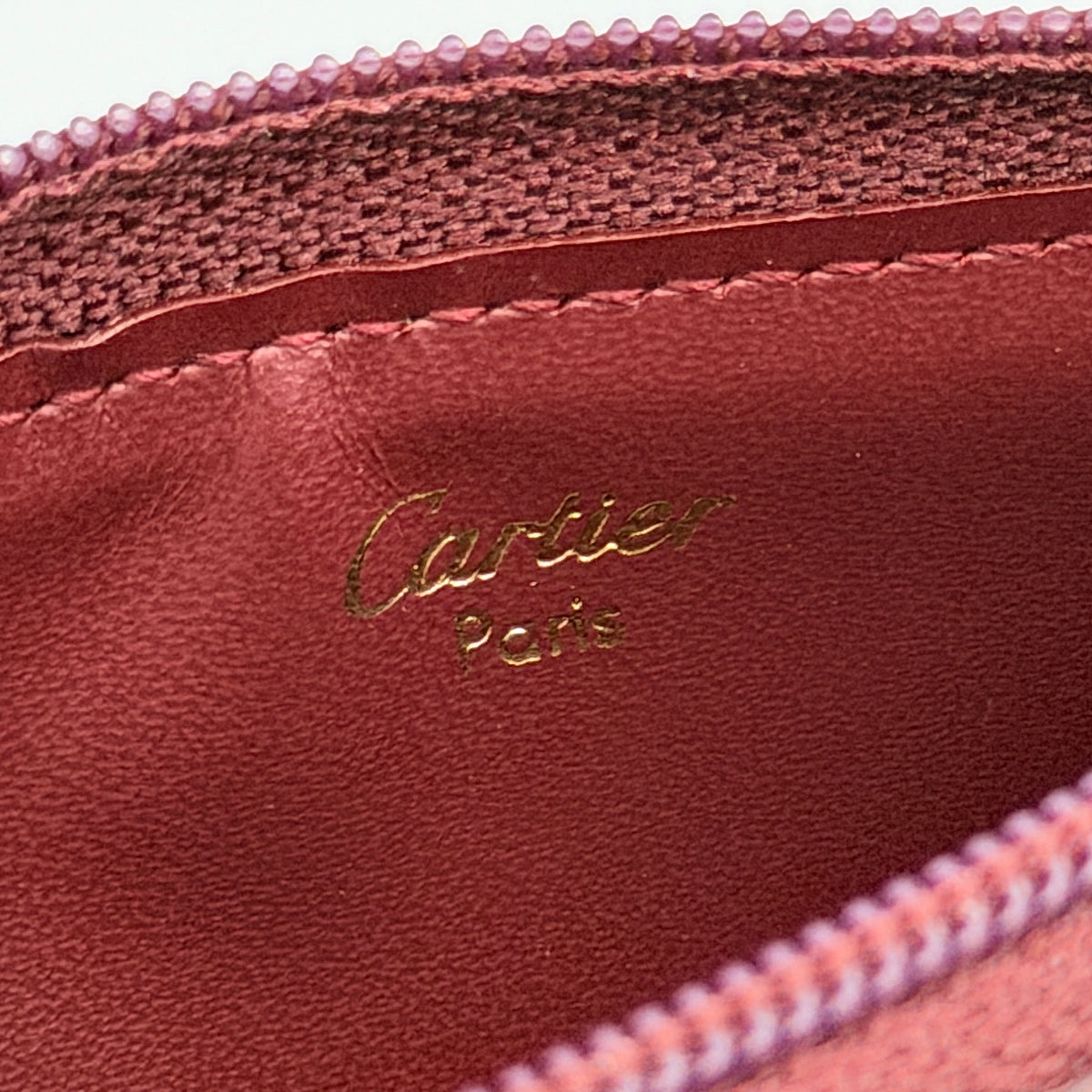 Cartier Must de Cartier burgundy leather coin purse with gold chain key holder and embossed logo, photographed on white.