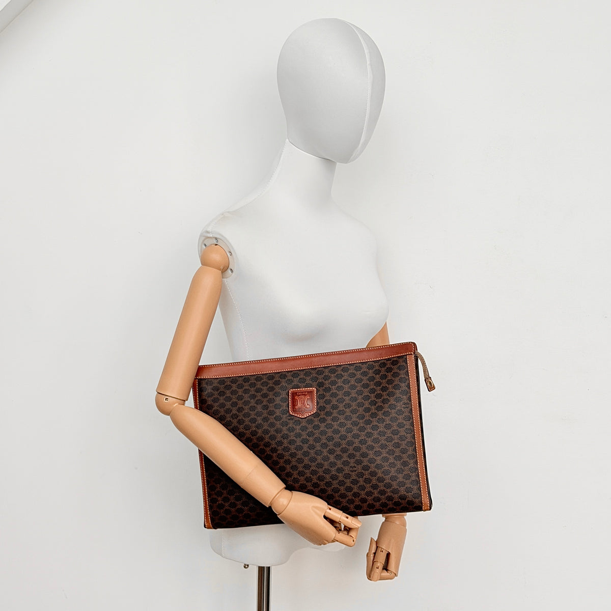 Celine Triomphe Macadam Clutch Bag in brown coated canvas with leather trim, shown against a white background.