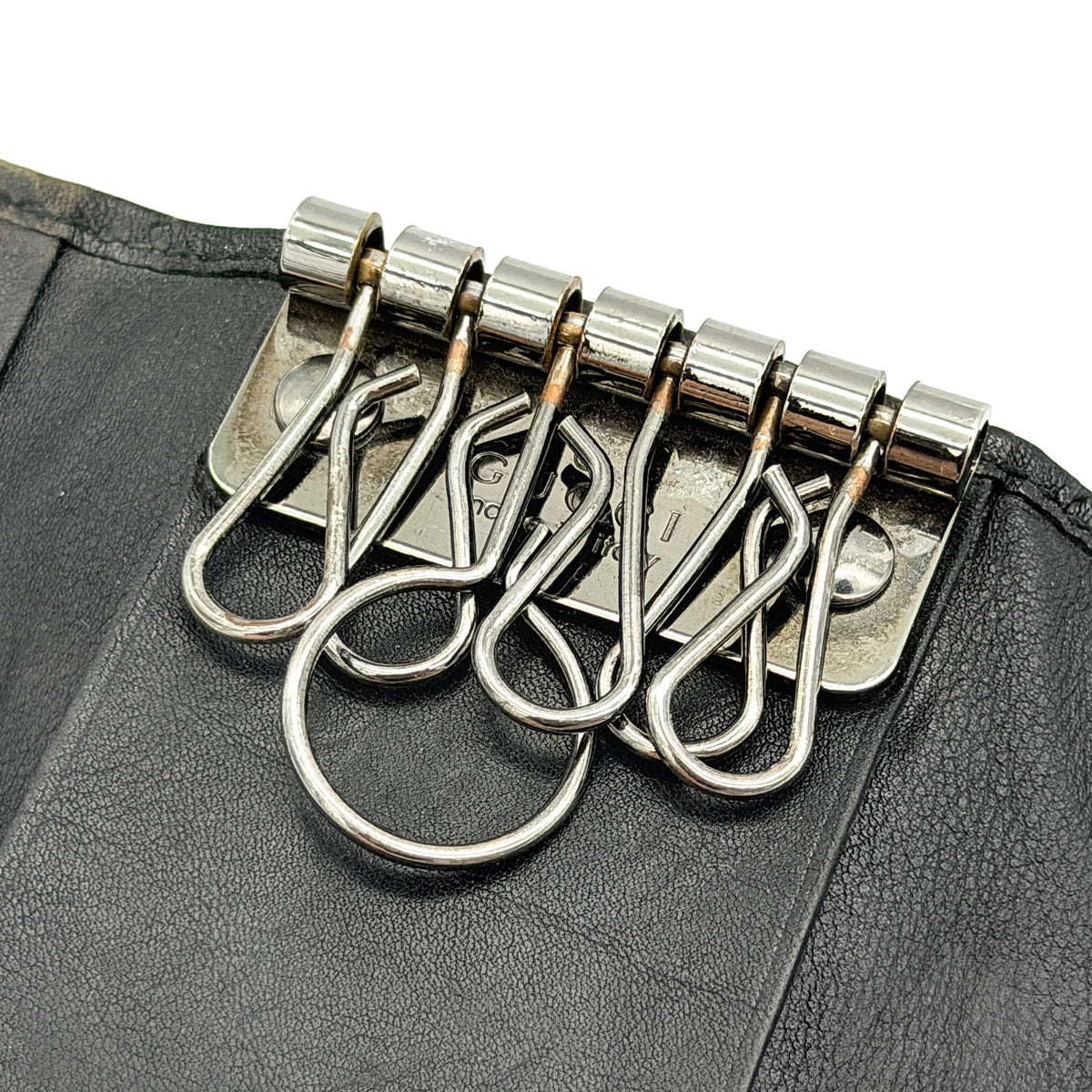Gucci Guccissima GG Monogram black leather key case with silver-tone hardware, shown closed against a white background.