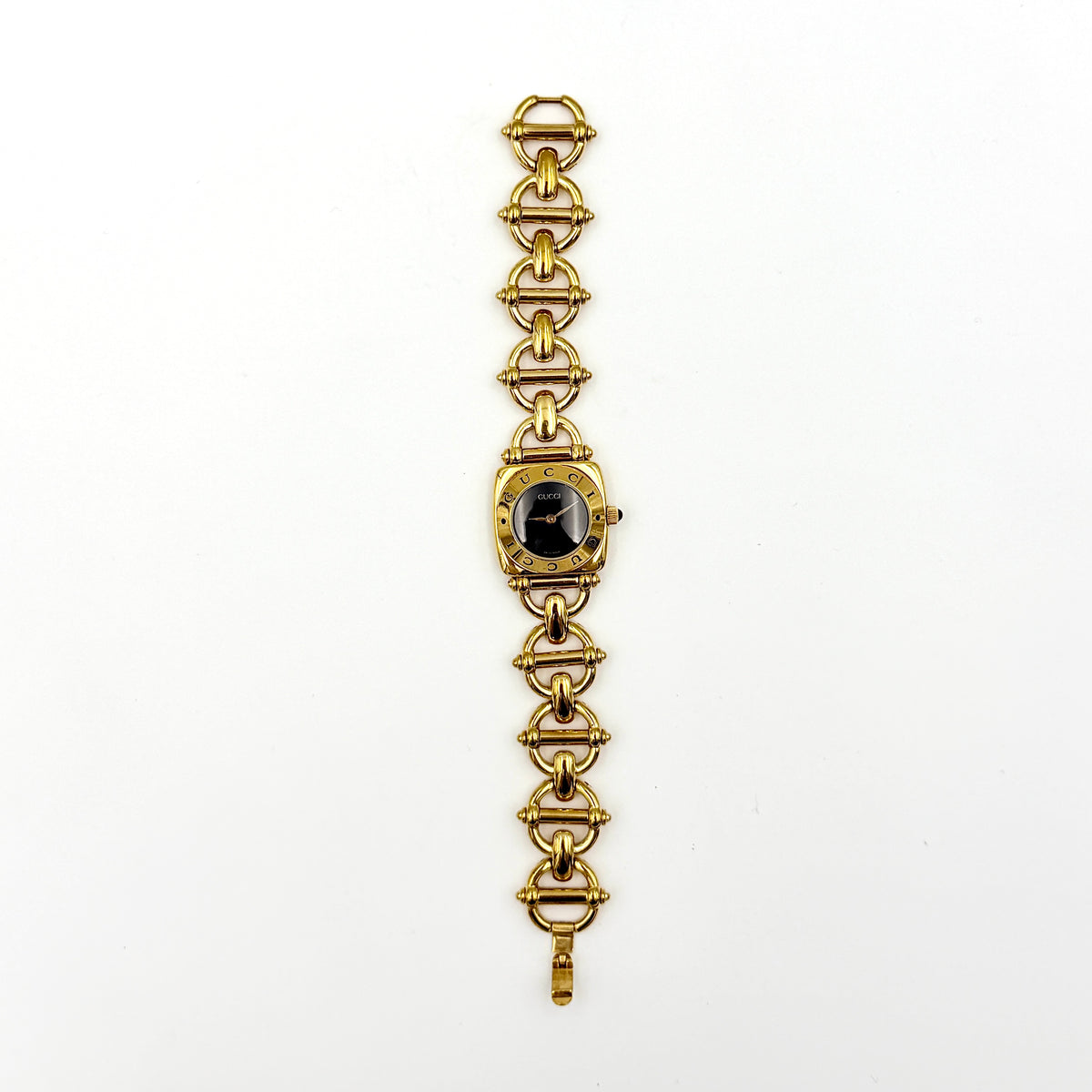Gucci 6400L gold-tone bracelet watch with a black dial and distinctive horsebit links, showcased on a clear stand.