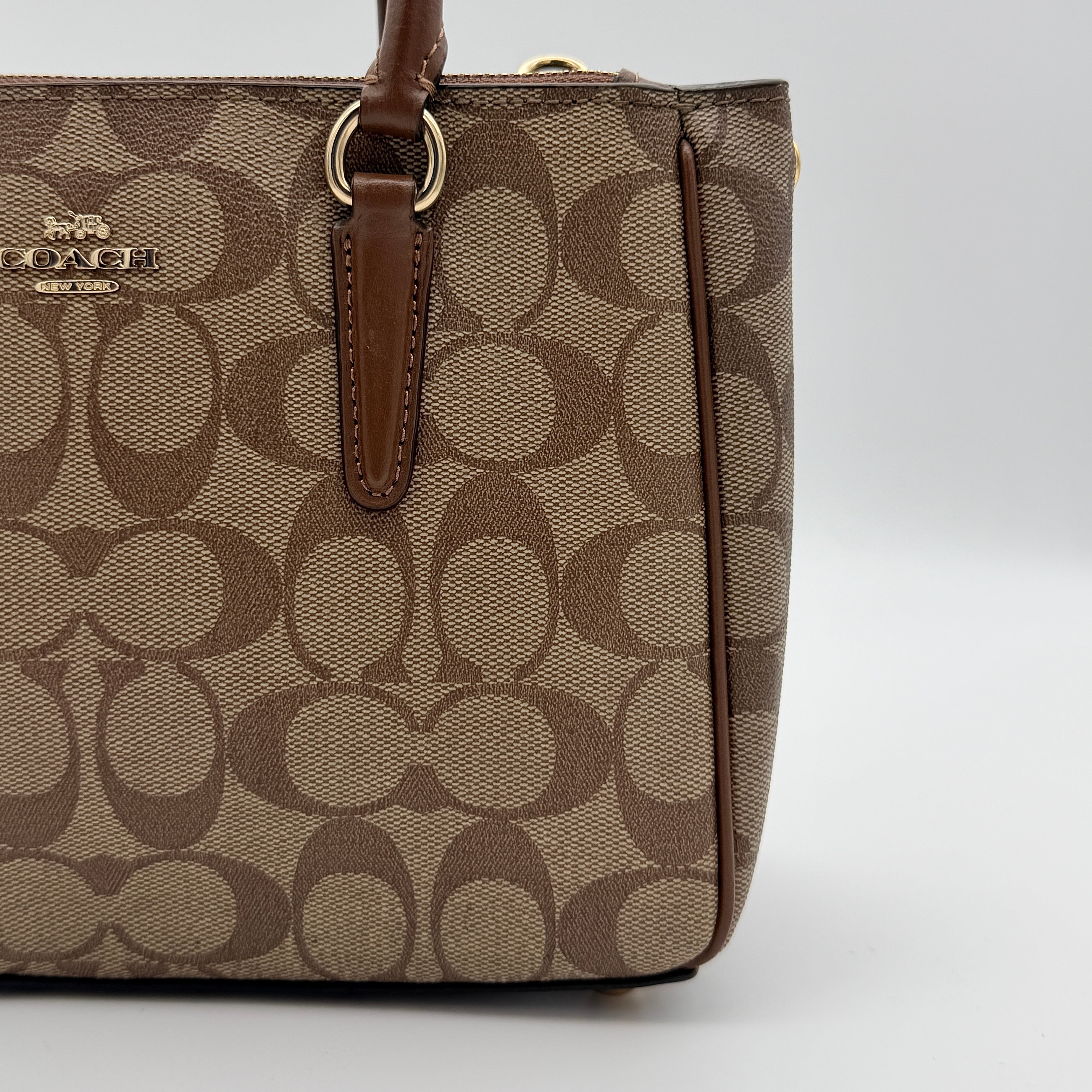 Coach Christie Carryall in beige and brown canvas with gold hardware and detachable strap, photographed in a studio setting.