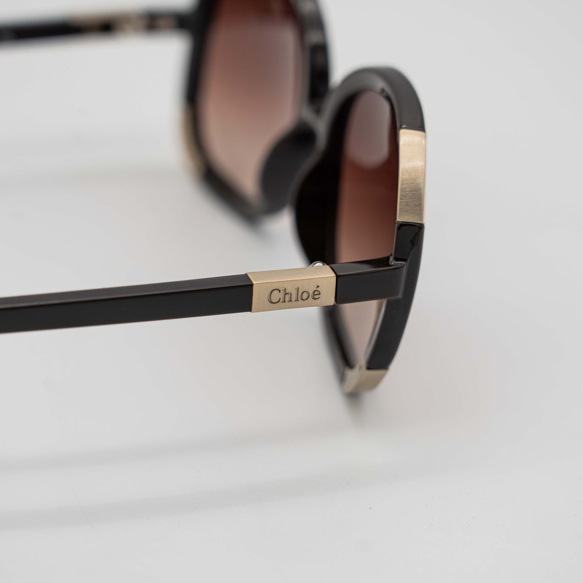 Chloé CL2119 sunglasses in black with gold-tone accents and brown gradient lenses, displayed at an angle.
