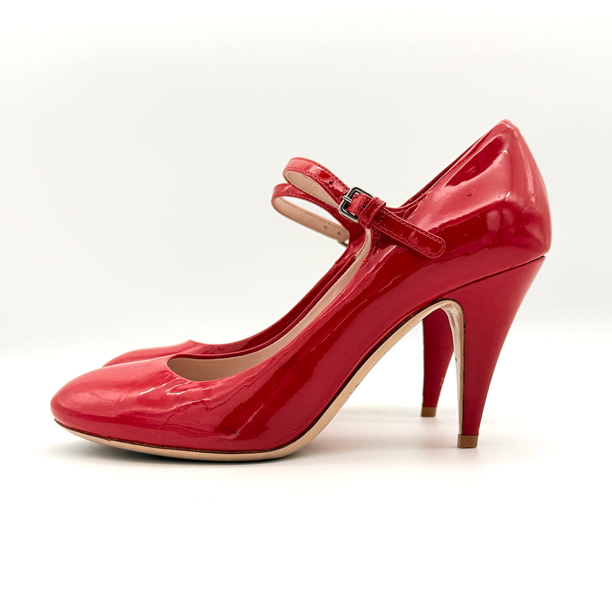 A pair of red patent leather Miu Miu Mary Jane heels with adjustable buckle straps and high heels, displayed against a white background.
