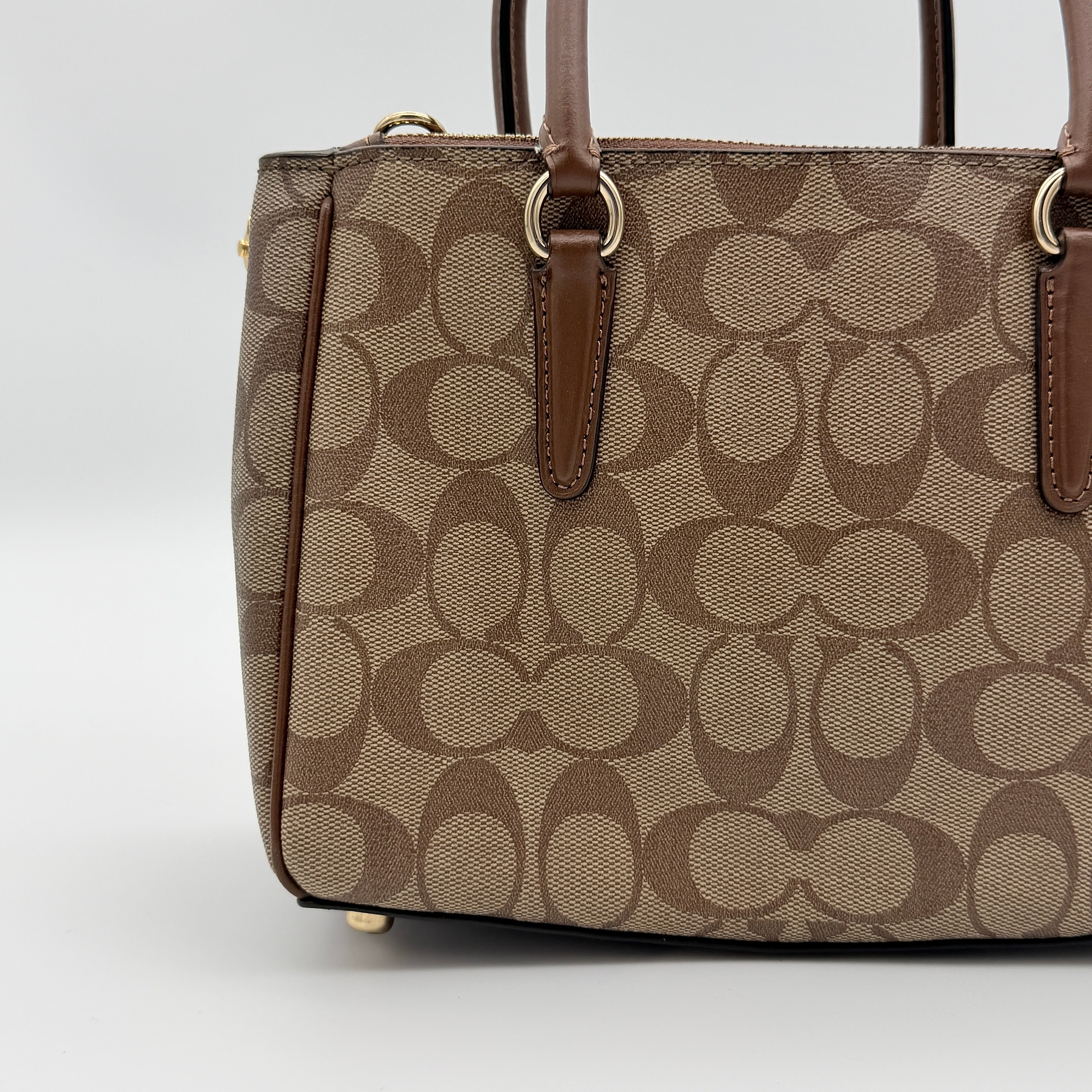 Coach Christie Carryall in beige and brown canvas with gold hardware and detachable strap, photographed in a studio setting.