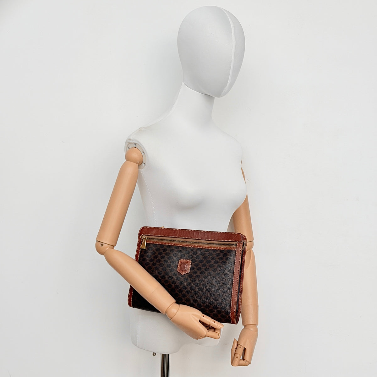 Celine Triomphe Macadam clutch bag in brown canvas with tan leather trim and gold hardware, shown with wrist strap.